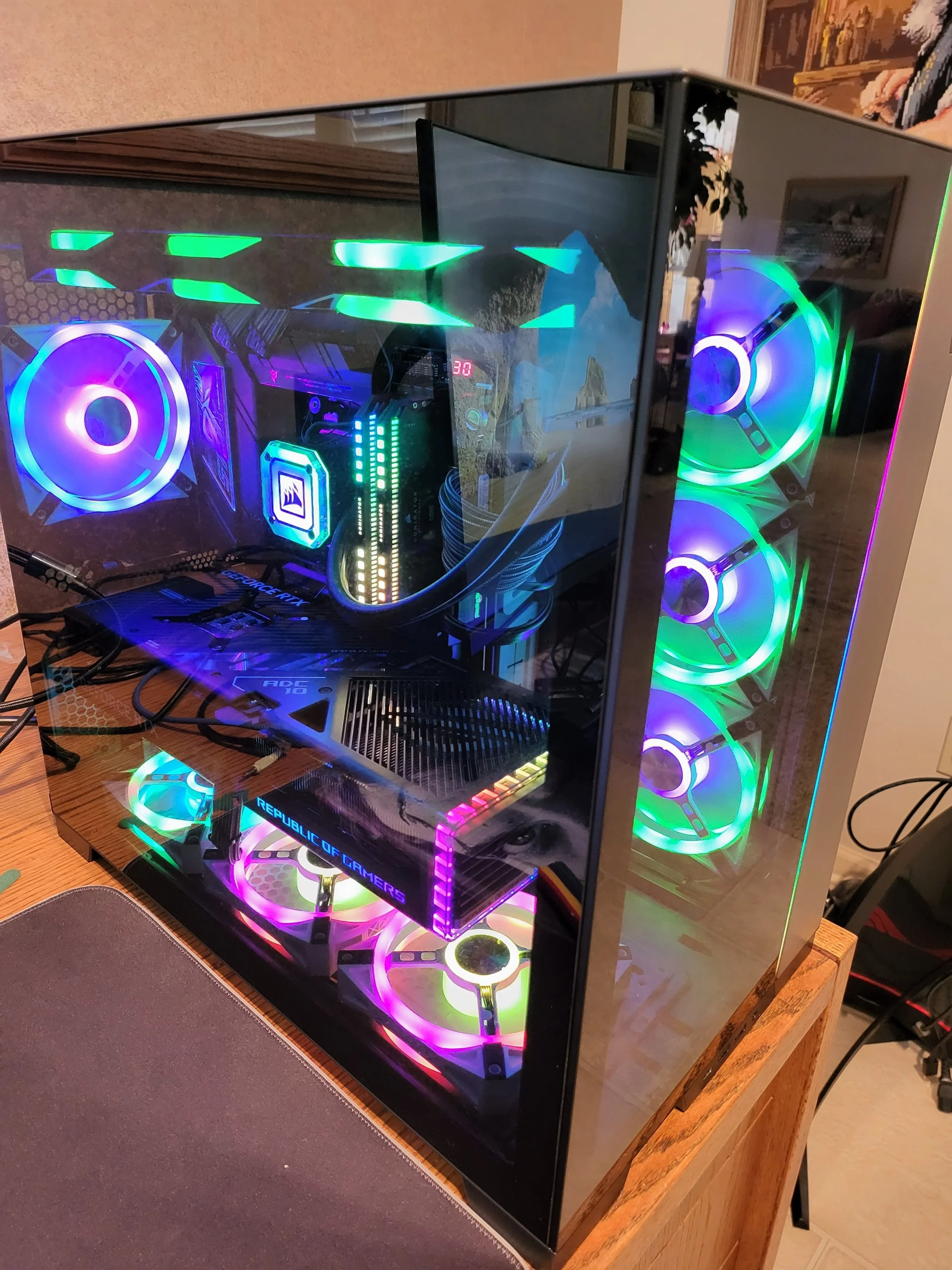A gaming computer with a glass case showing interior components, illuminated with colorful RGB lighting, including fans, RAM, and cooling system.