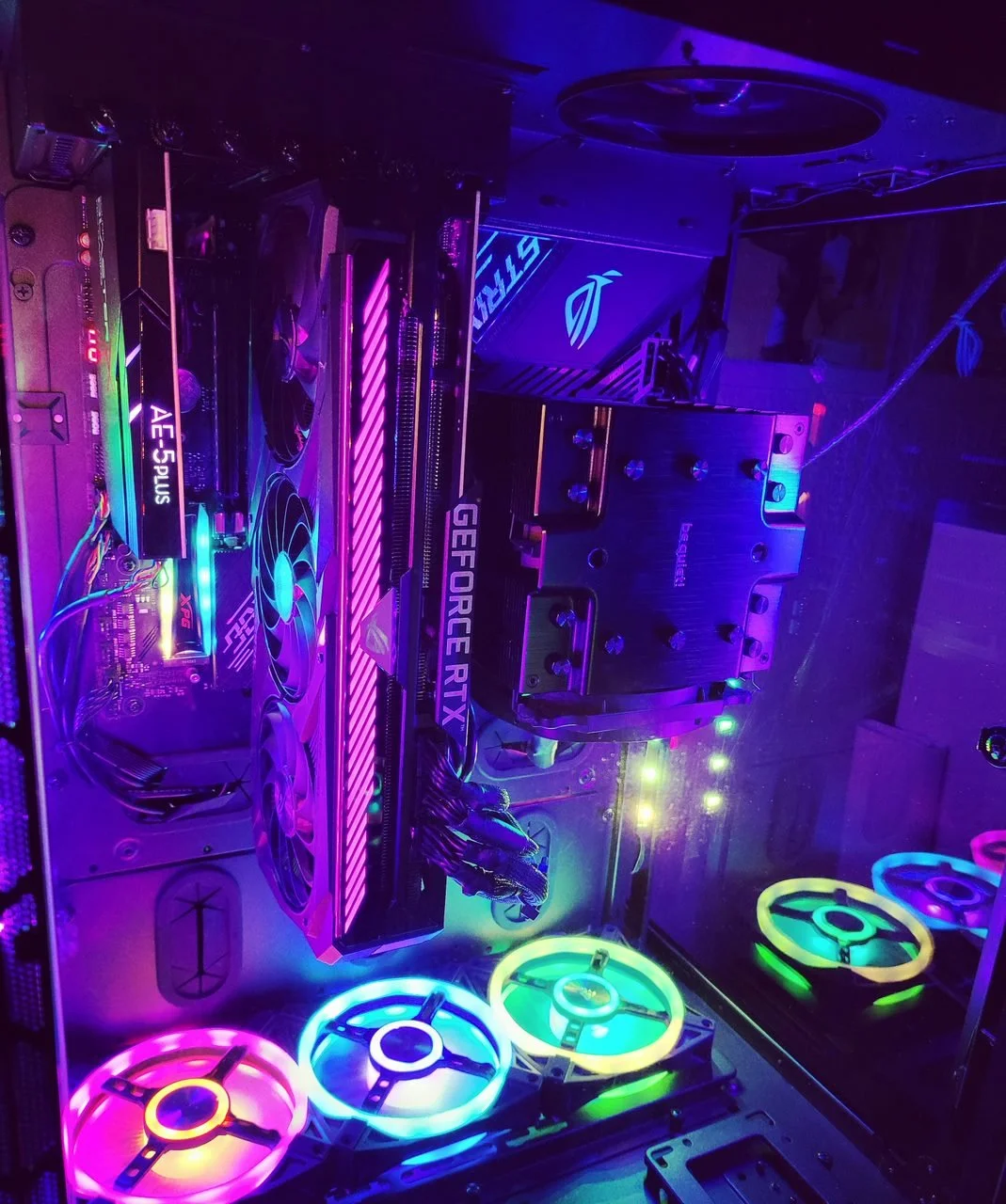 Inside a gaming PC with colorful RGB lighting, featuring a graphics card, CPU cooler, RAM, and illuminated fans.