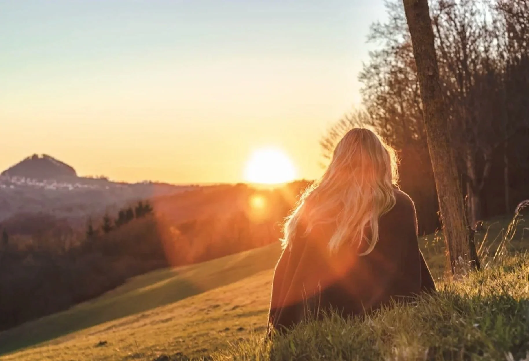 woman contemplating life while sitting in a meadow at sunset