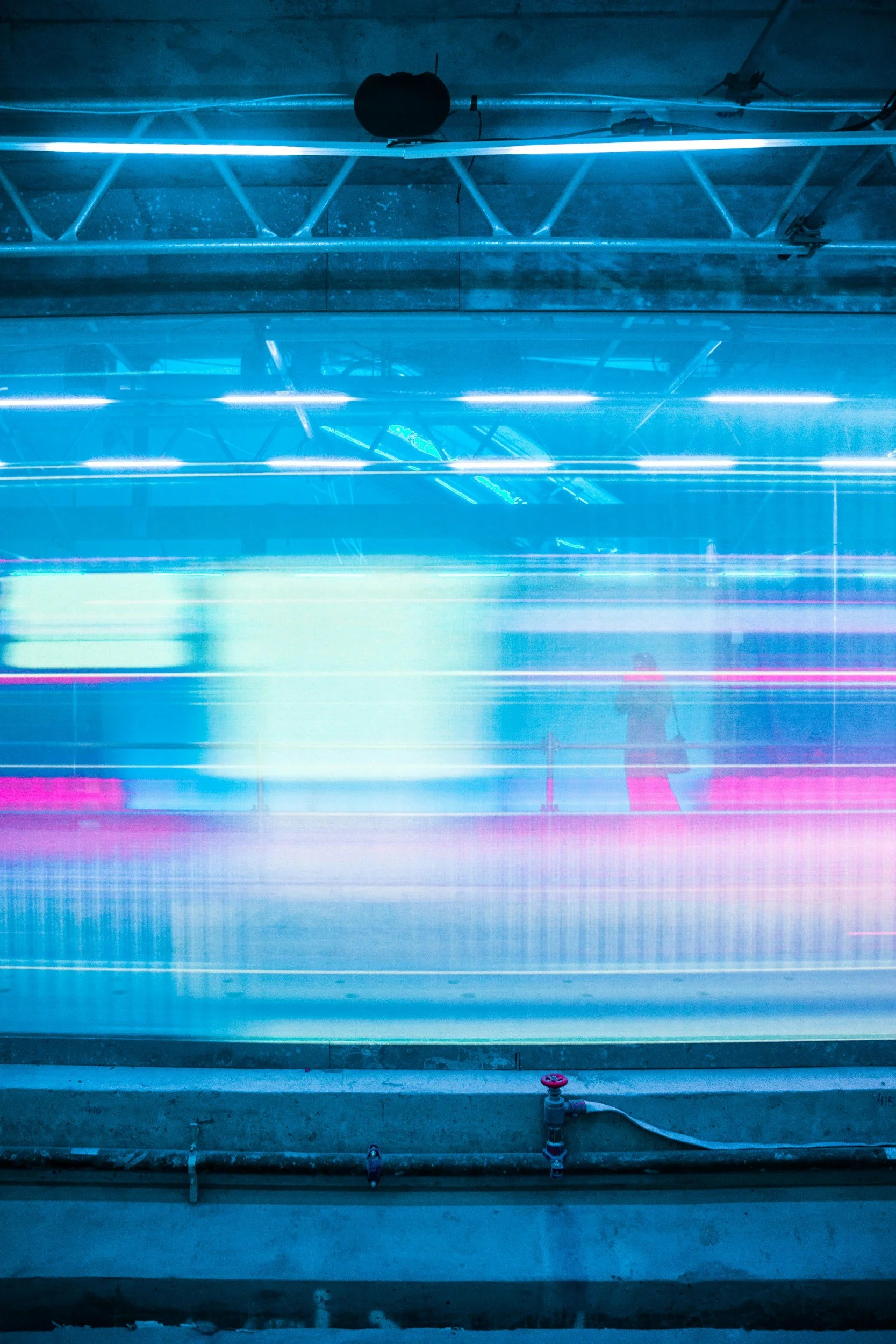 Long exposure photo of a person walking past colorful neon lights, creating streaks of light in an indoor space.