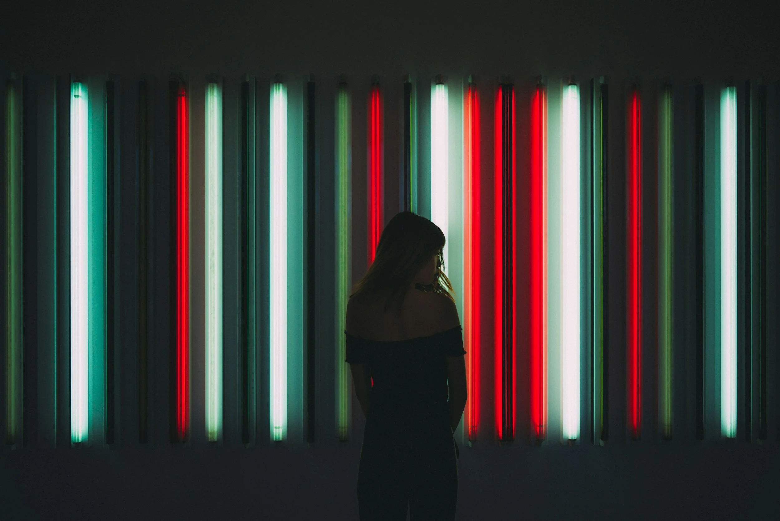 Silhouette of a woman standing in front of a colorful neon light installation with vertical red, white, and green lights.