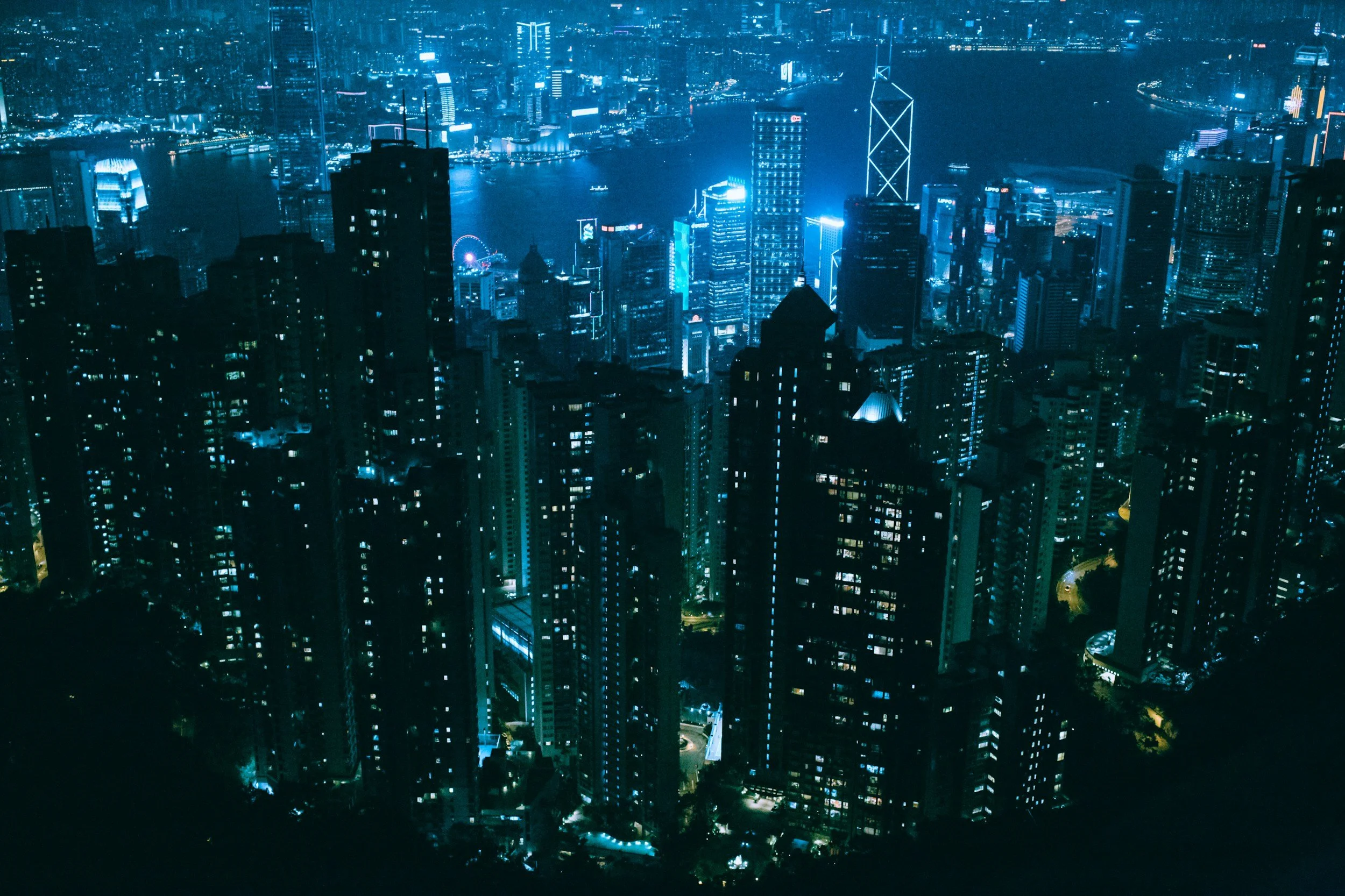 Night view of a cityscape with illuminated skyscrapers and a river in the background.