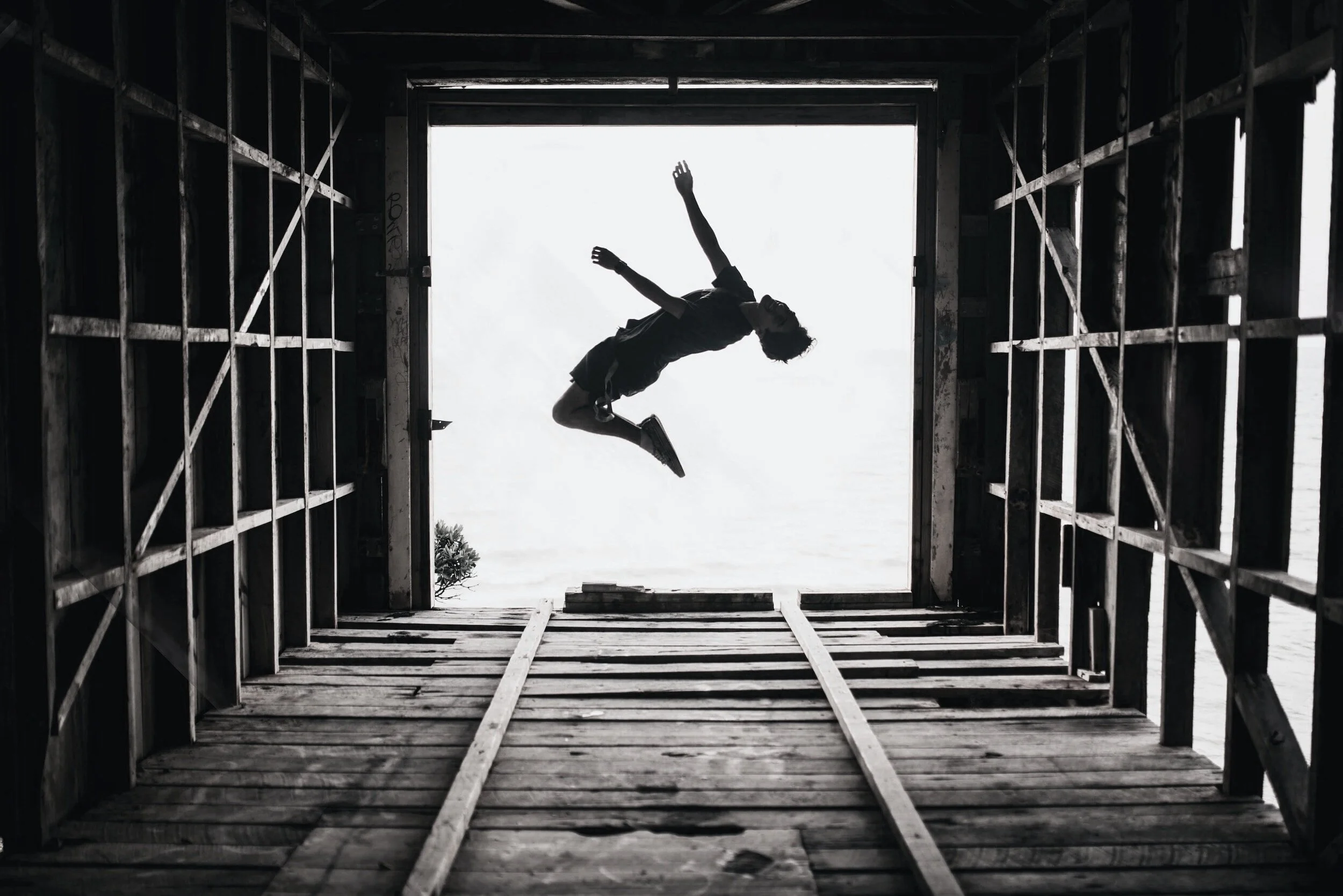 A silhouette of a person jumping in mid-air inside a wooden structure with an opening overlooking the sky.