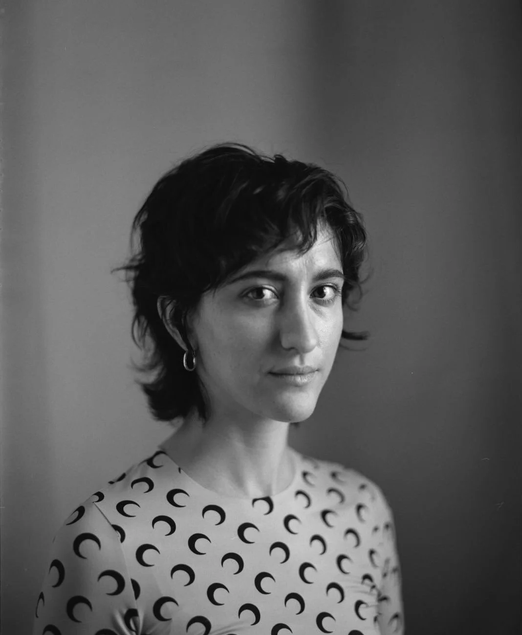 Black and white portrait of a woman with short, wavy hair wearing a patterned top with circles and small hoop earrings.