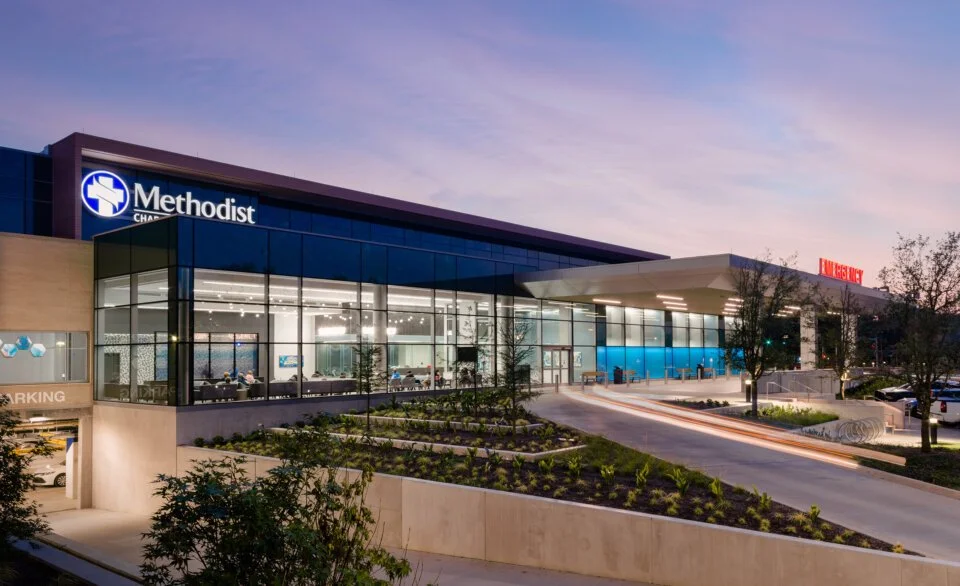 Contemporary Methodist Hospital facility in Dallas, Texas with large glass curtain wall, covered drop-off canopy, and landscaped entry drive at sunset.