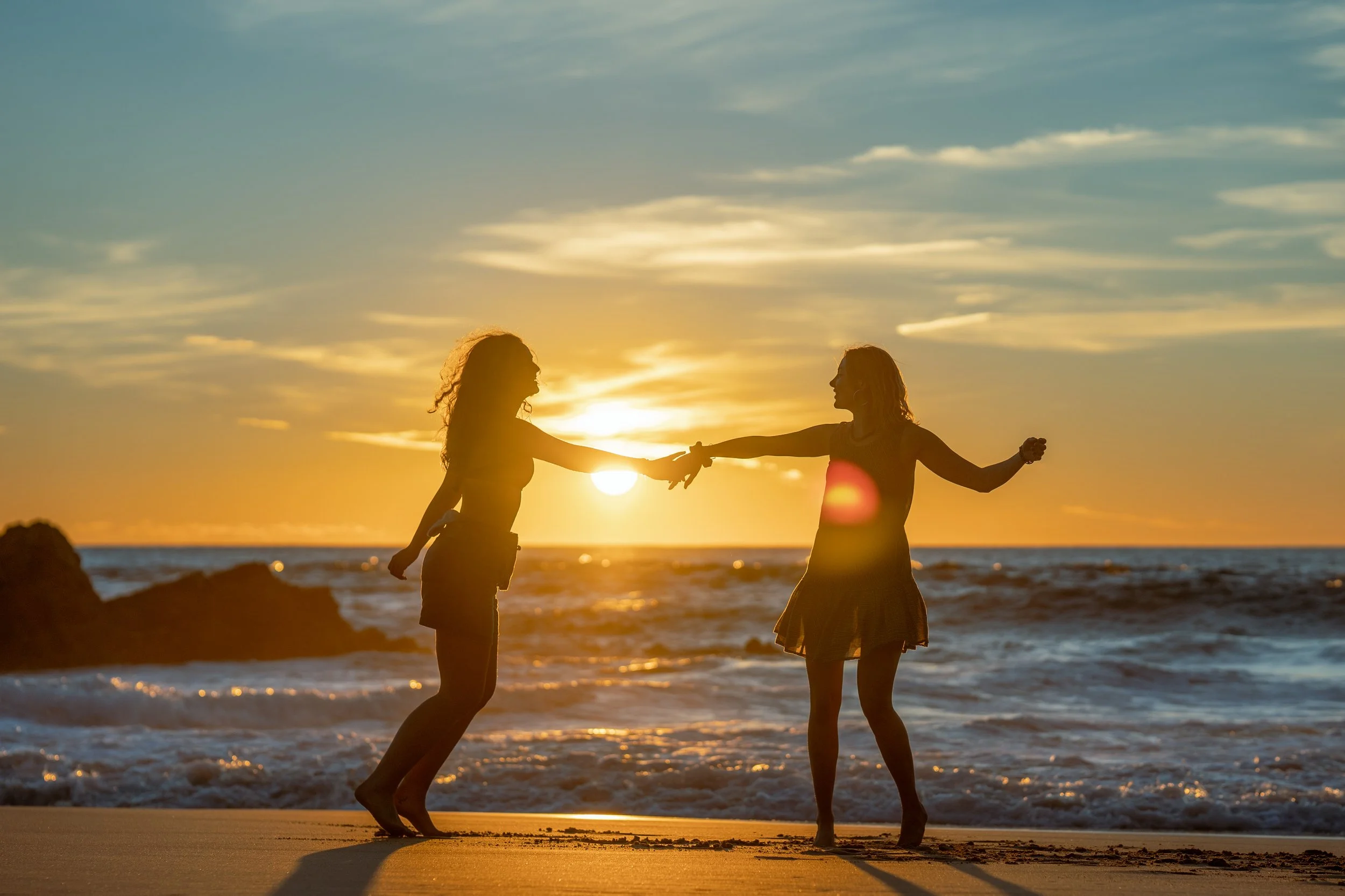 Two girls dancing on the beach during sunset