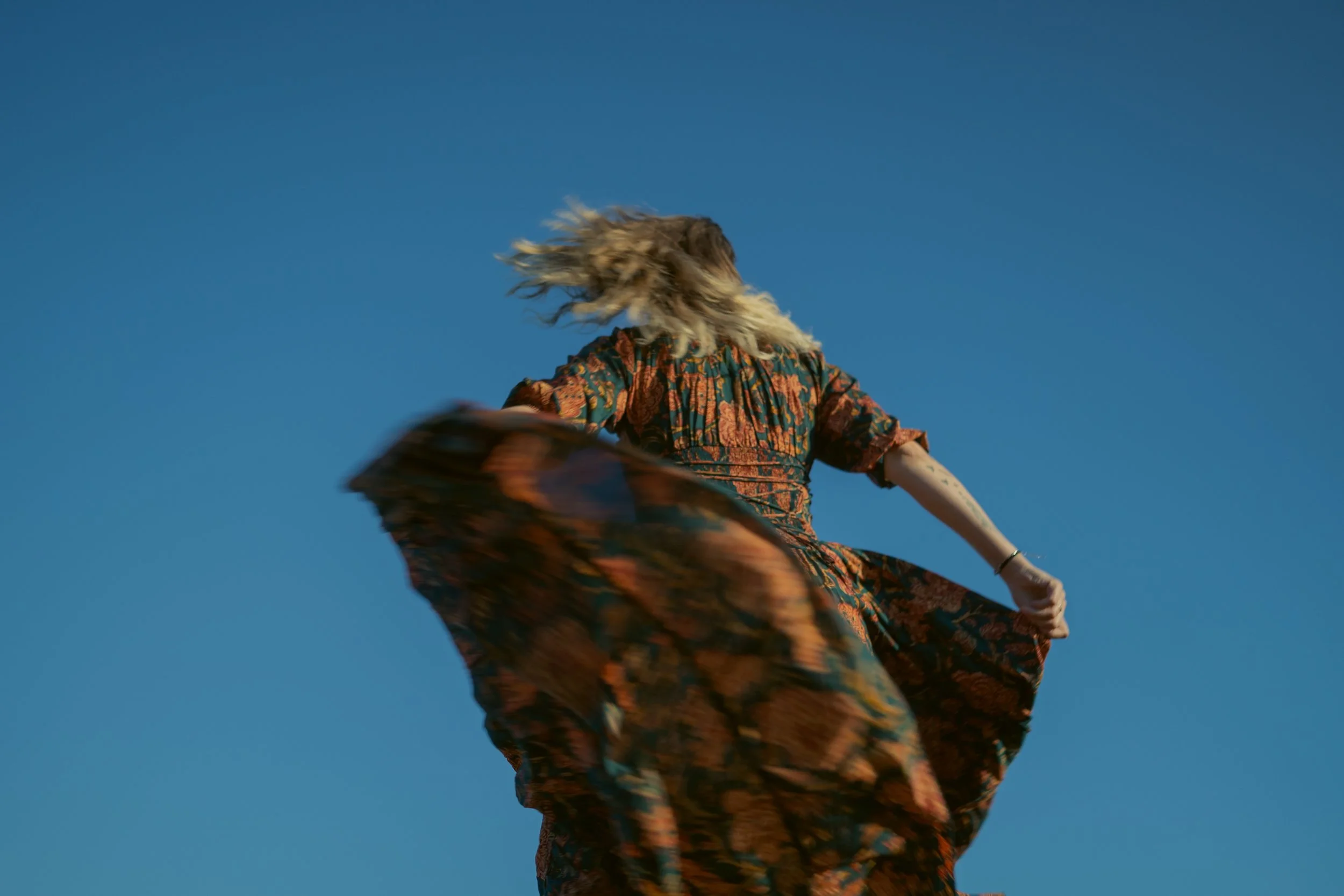Girl dancing with long dress in front of blue sky