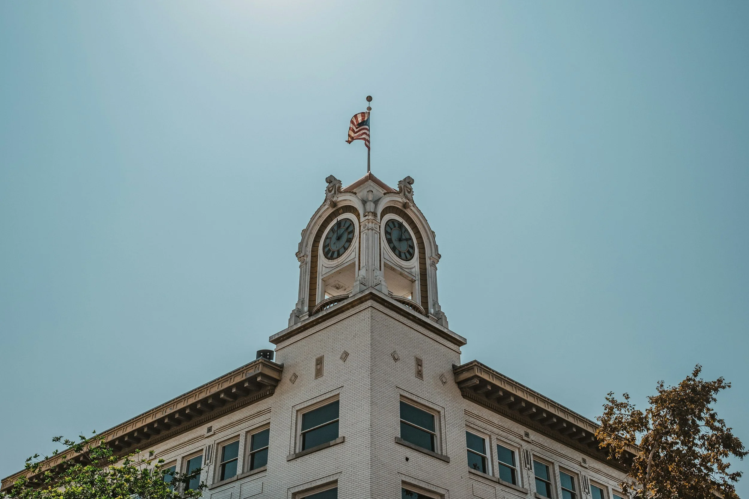 A historic building with a clock tower and an American flag on top, against a clear blue sky.
