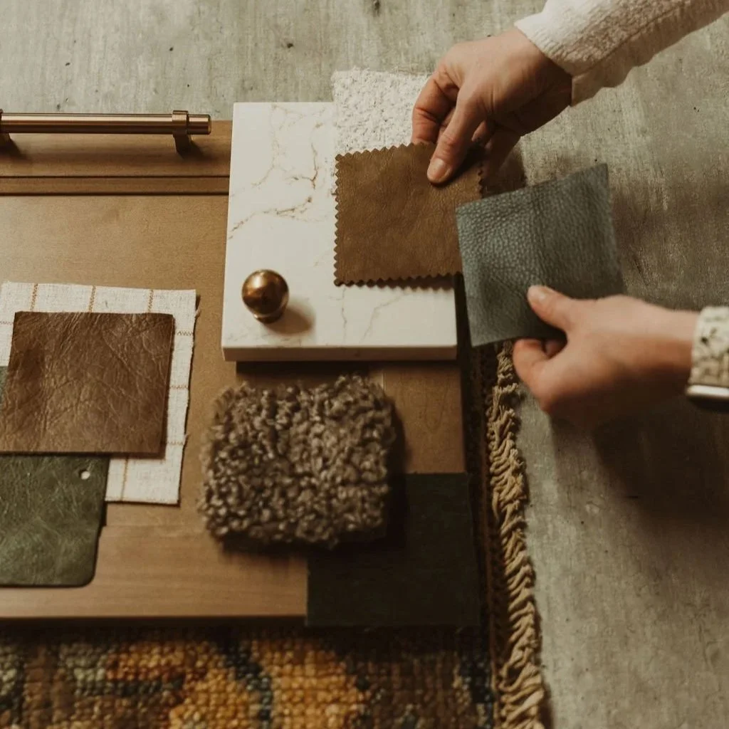 Person comparing different fabric swatches on a table, including leather and textured materials, in a design setting.