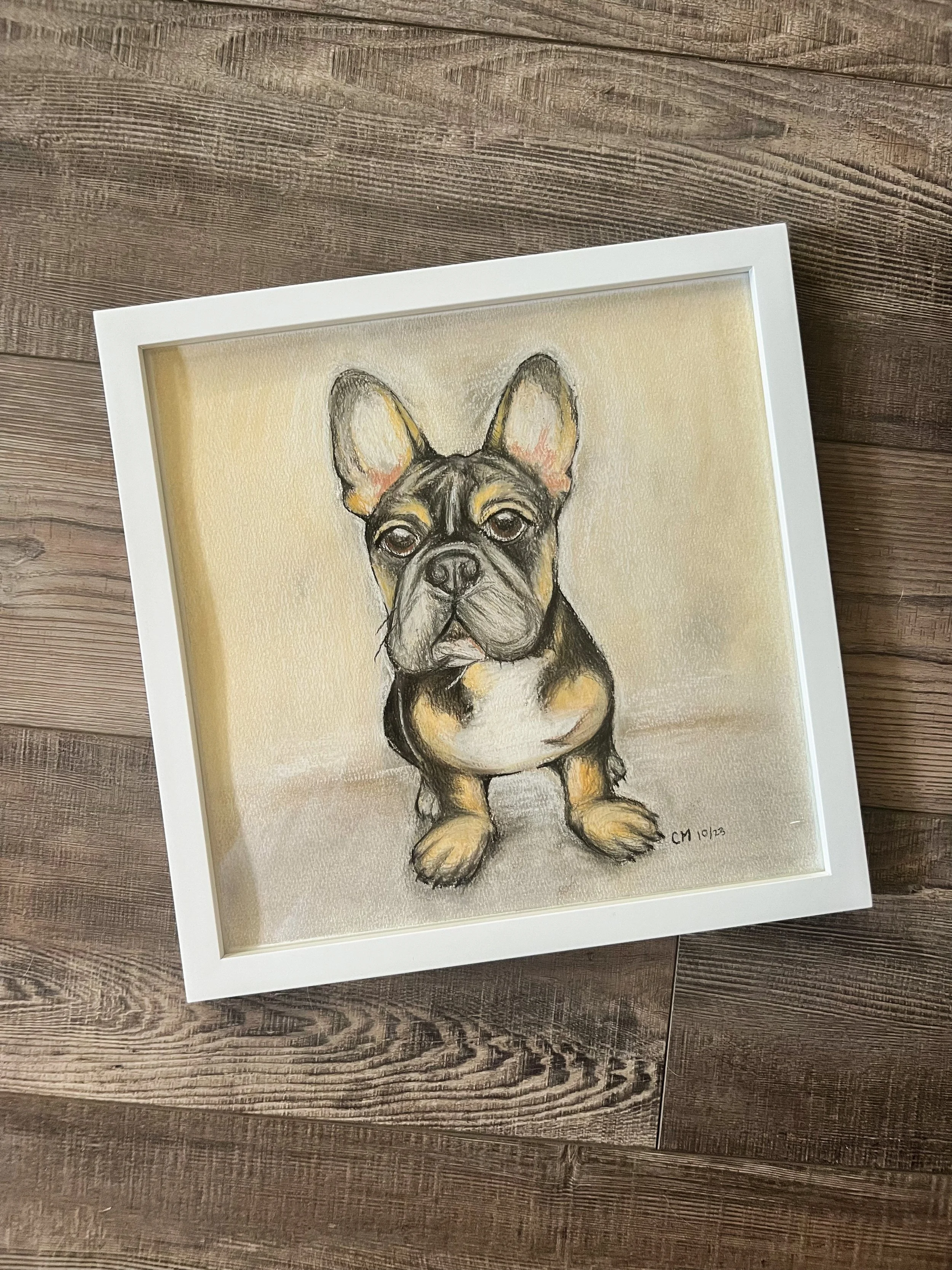 Framed painting of a French Bulldog puppy on a wooden surface.