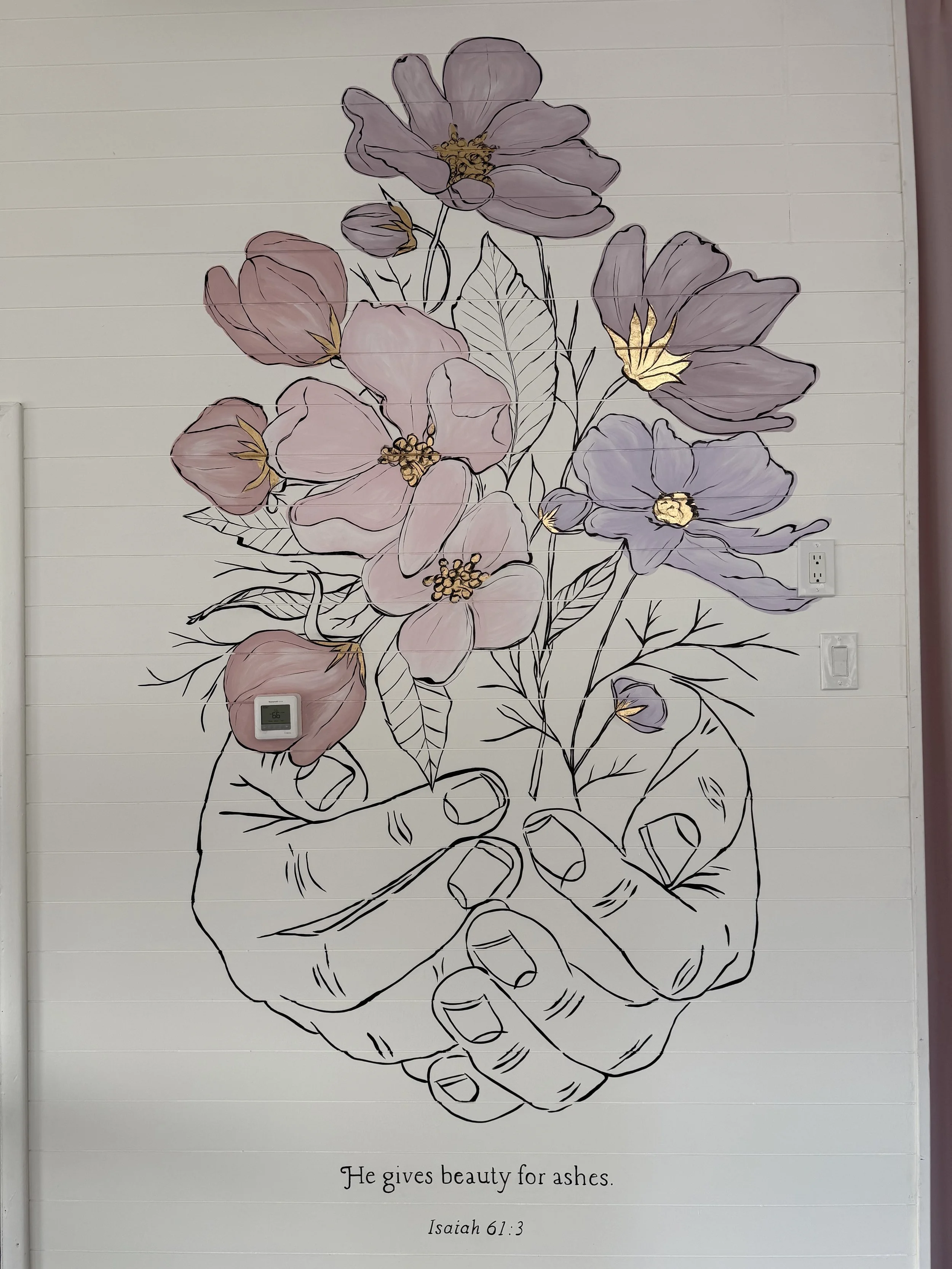 A line drawing of a hand holding a bouquet of blooming flowers, with some petals filled with pastel pink and purple colors and gold accents, on a wall with electrical outlets. Below, there is a quote reading 'He gives beauty for ashes' with a biblical reference to Isaiah 61:3.