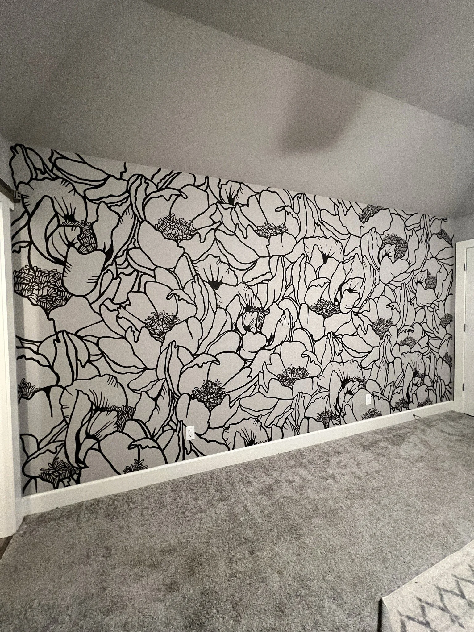 A wall decorated with black and white floral wallpaper in a room with gray carpeting.