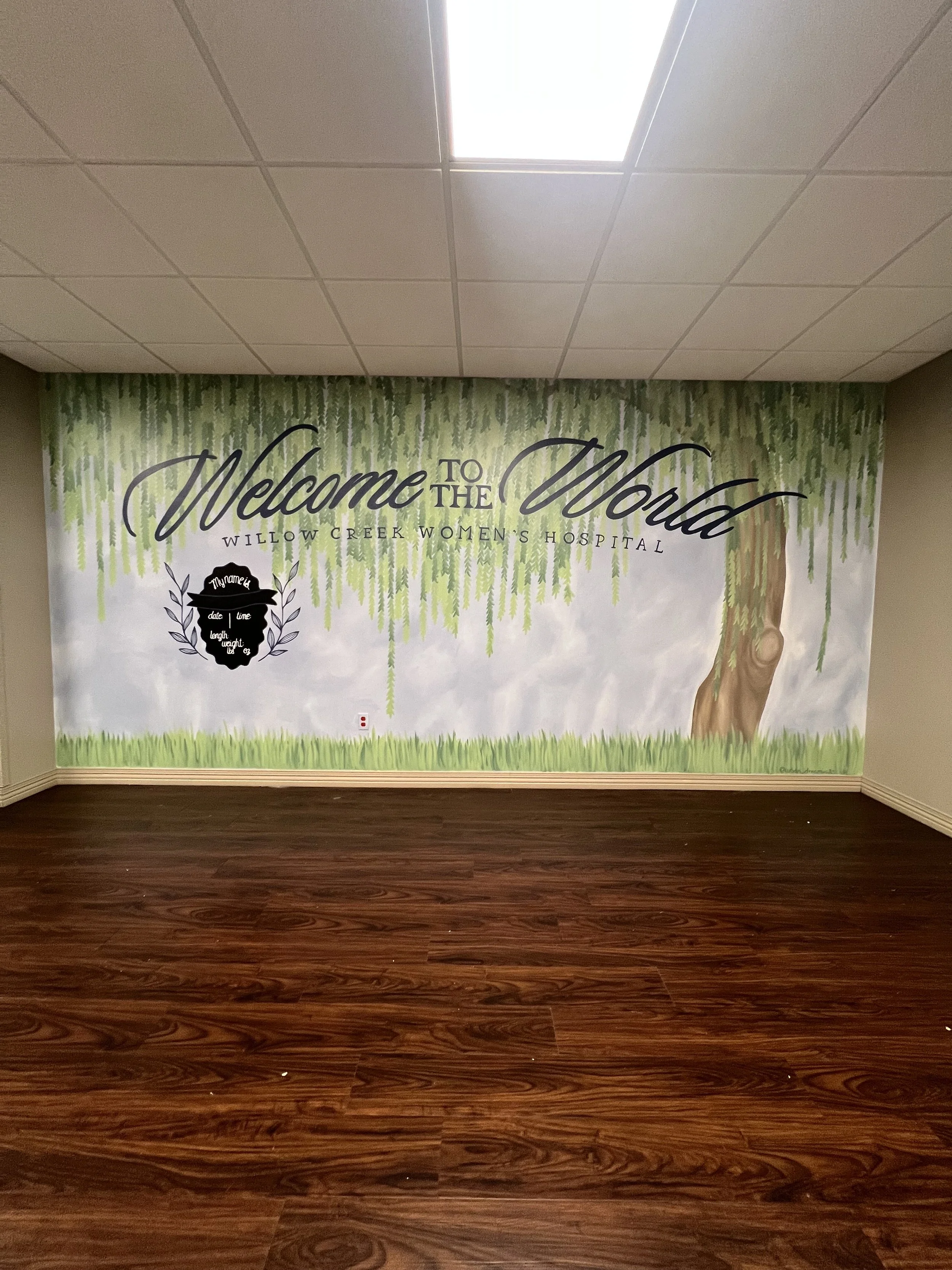 A mural on a wall welcoming visitors to Willow Creek Women's Hospital with a painted tree and hanging branches at the top.