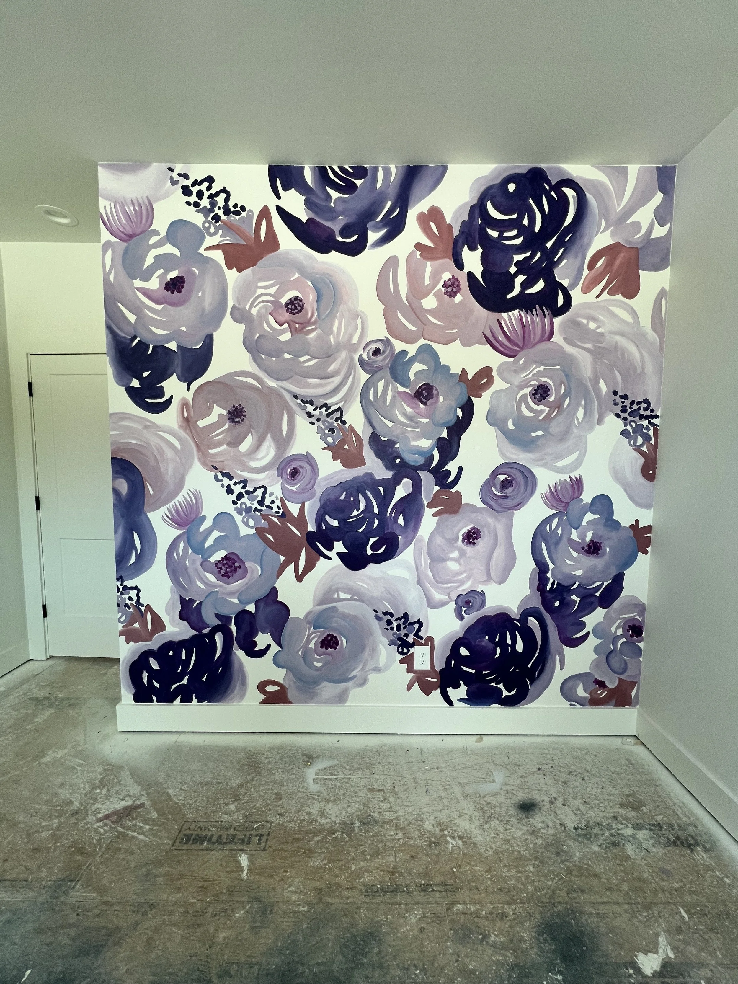 A large, colorful painted floral mural on an interior wall featuring abstracted purple, pink, white, and blue flowers with dark accents, situated in a modern room with a partially unfinished floor.