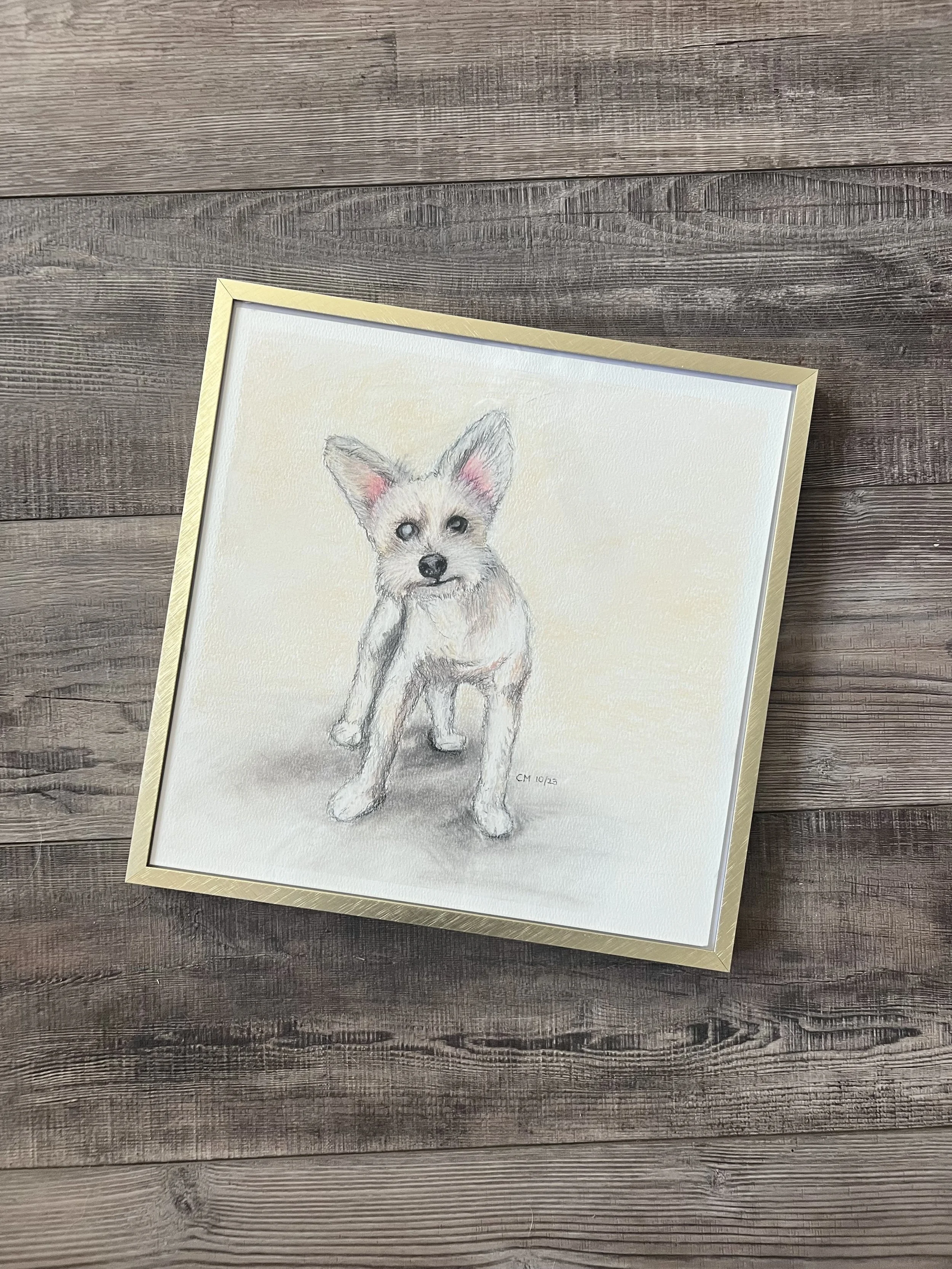 Framed watercolor painting of a small, light-colored dog with large ears, sitting against a neutral background on a wooden surface.