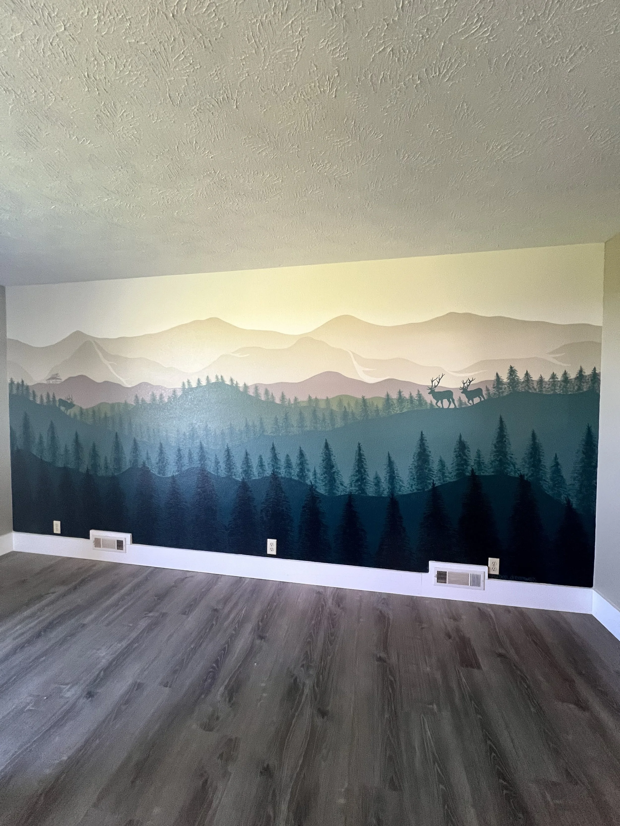 A living room with a mountain landscape mural painted on the wall, featuring layered mountain ranges and pine trees, with two elk silhouettes near the top.