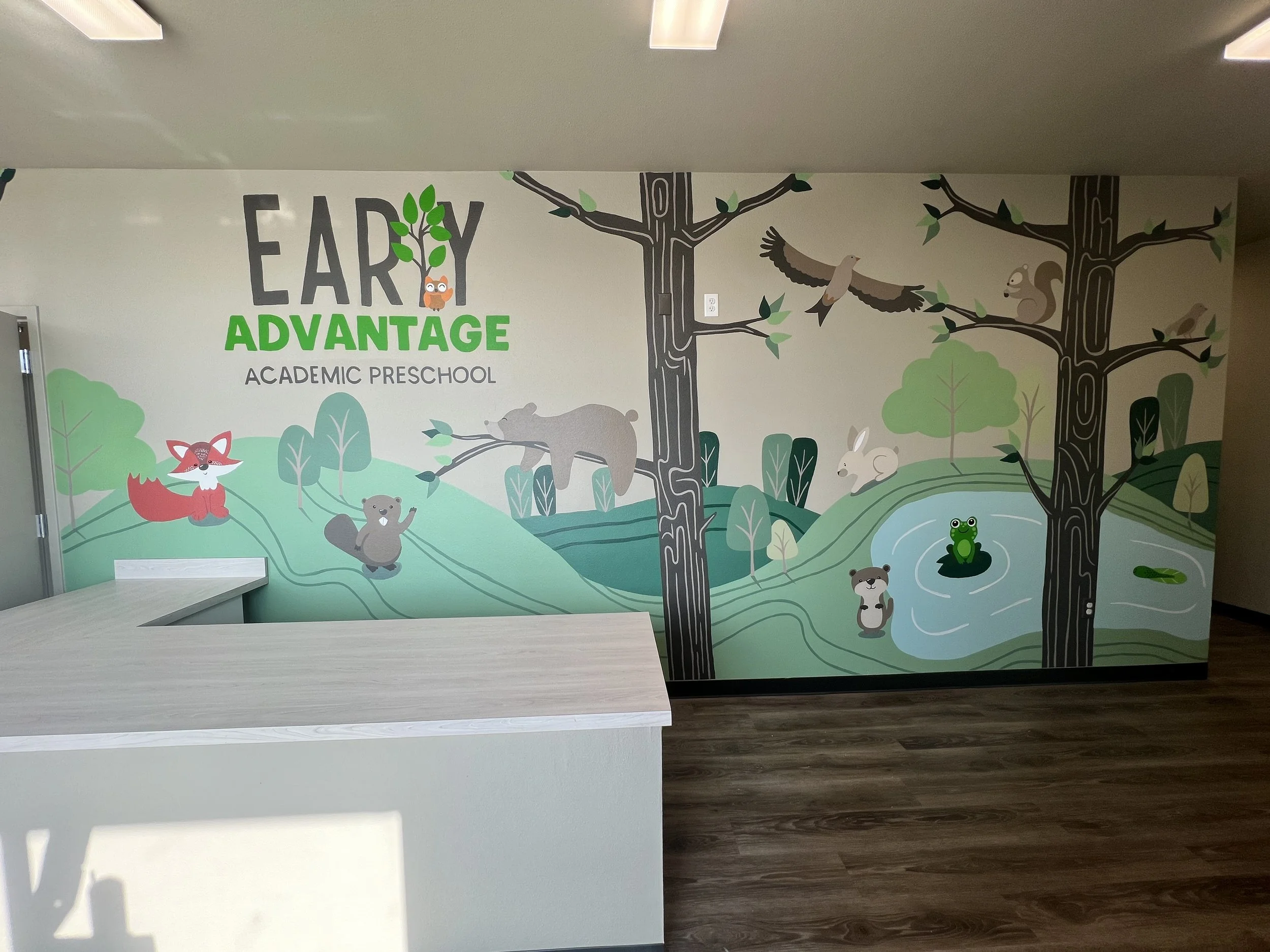 Colorful mural for an early childhood academic preschool featuring cartoon animals in a nature scene with trees, a pond with a frog, an eagle, a squirrel, a fox, a bear, a rabbit, and a bird, with the text 'Early Advantage Academic Preschool' centered at the top.