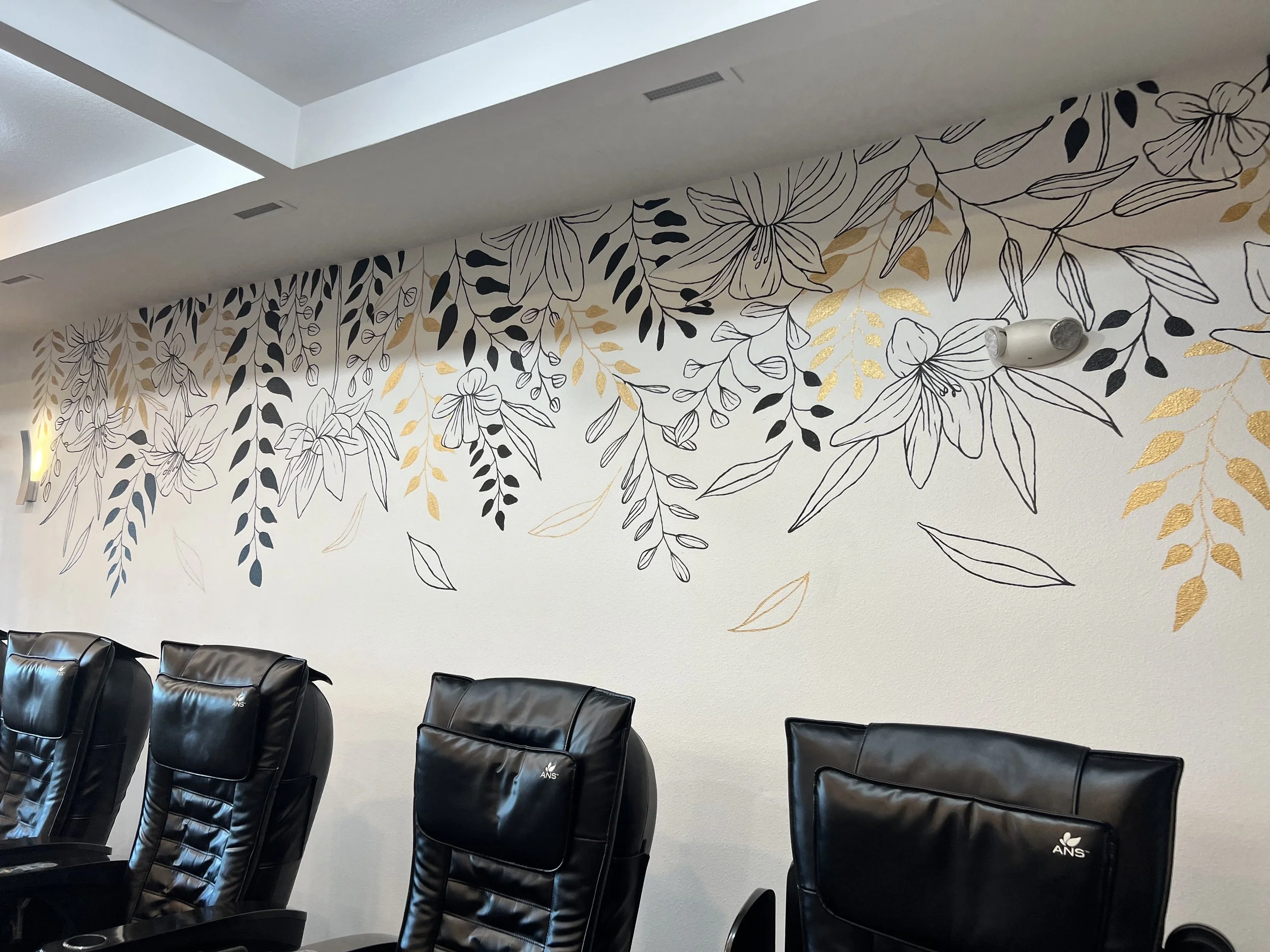 Interior of a conference room with black leather chairs in front of a white wall decorated with black and gold floral wallpaper design.