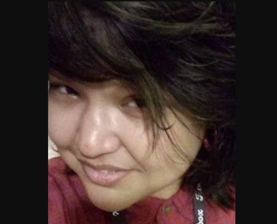 An Indigenous person with dark hair wearing a red button-up shirt.