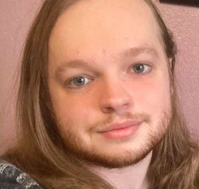 A white trans man with blue eyes and facial hair.