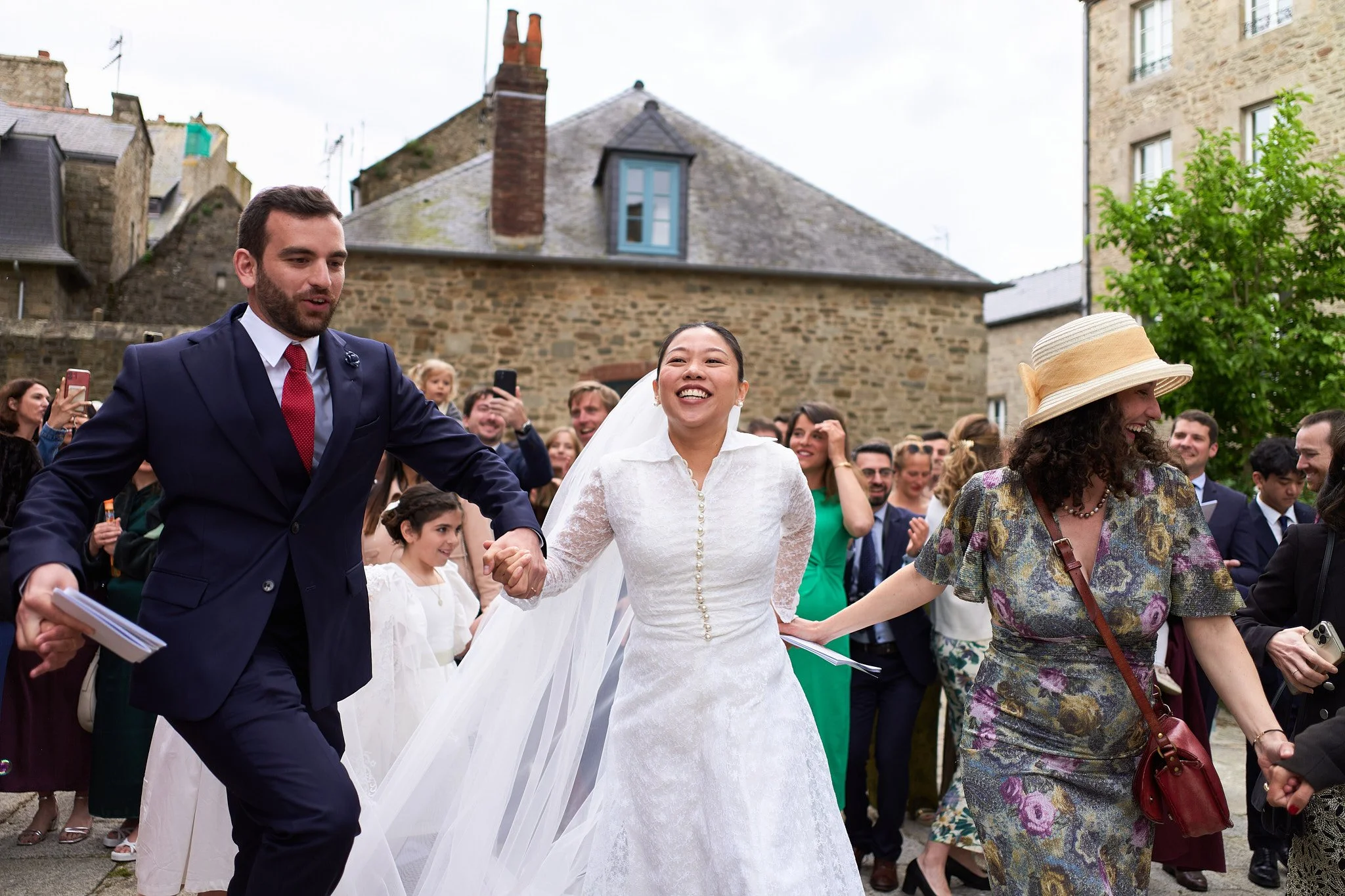 Mariée souriante en robe blanche entourée d'invités, lors d'un mariage extérieur.
