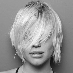 Close-up of a woman with a short, messy blonde hairstyle covering part of her face, black and white image.