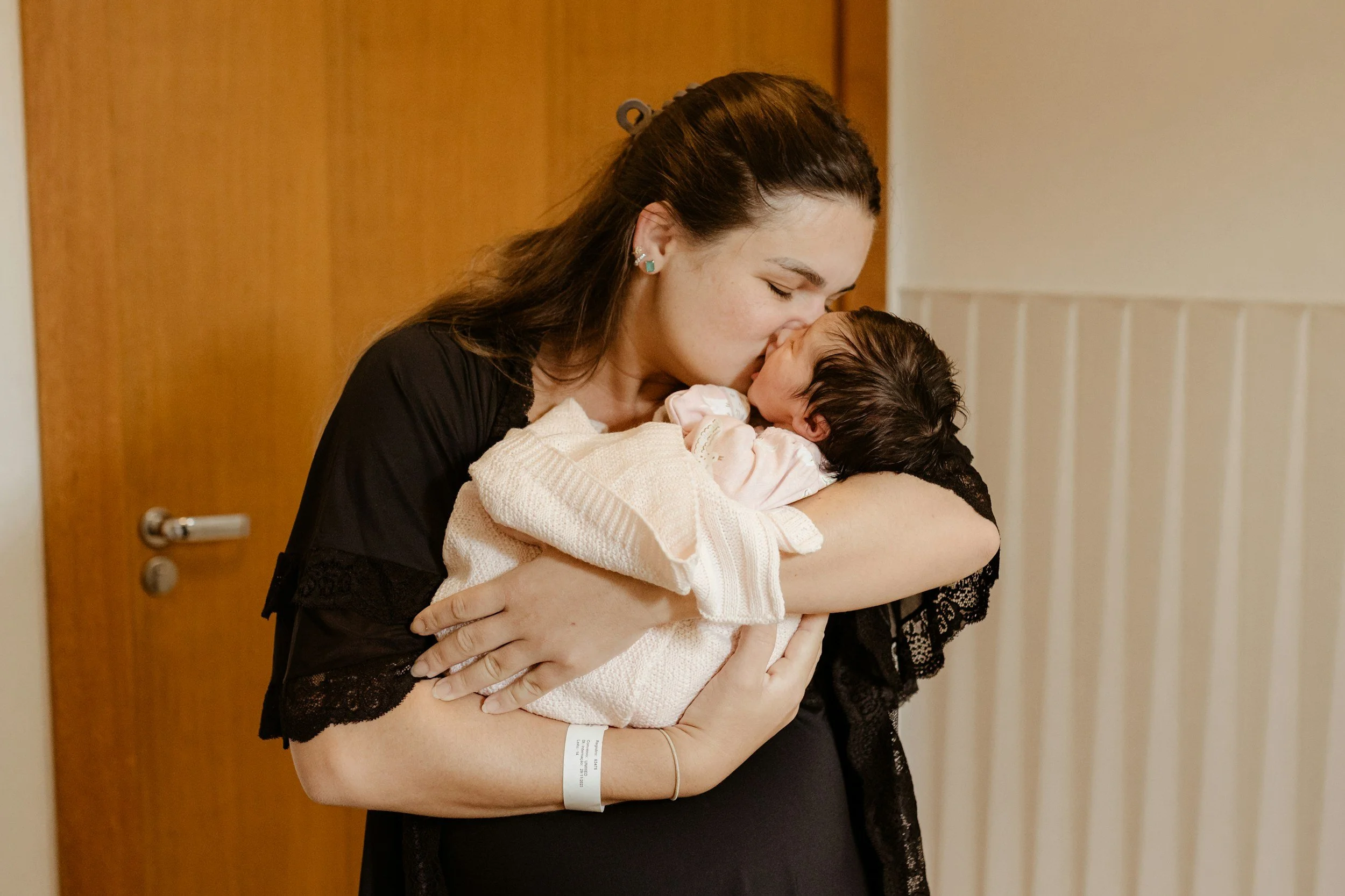 A woman holding and kissing a newborn baby.