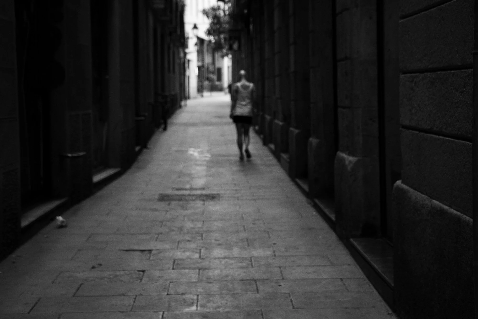 Woman walking away down a dark narrow street towards the light, Gothic Quarter Barcelona — Leica Q3