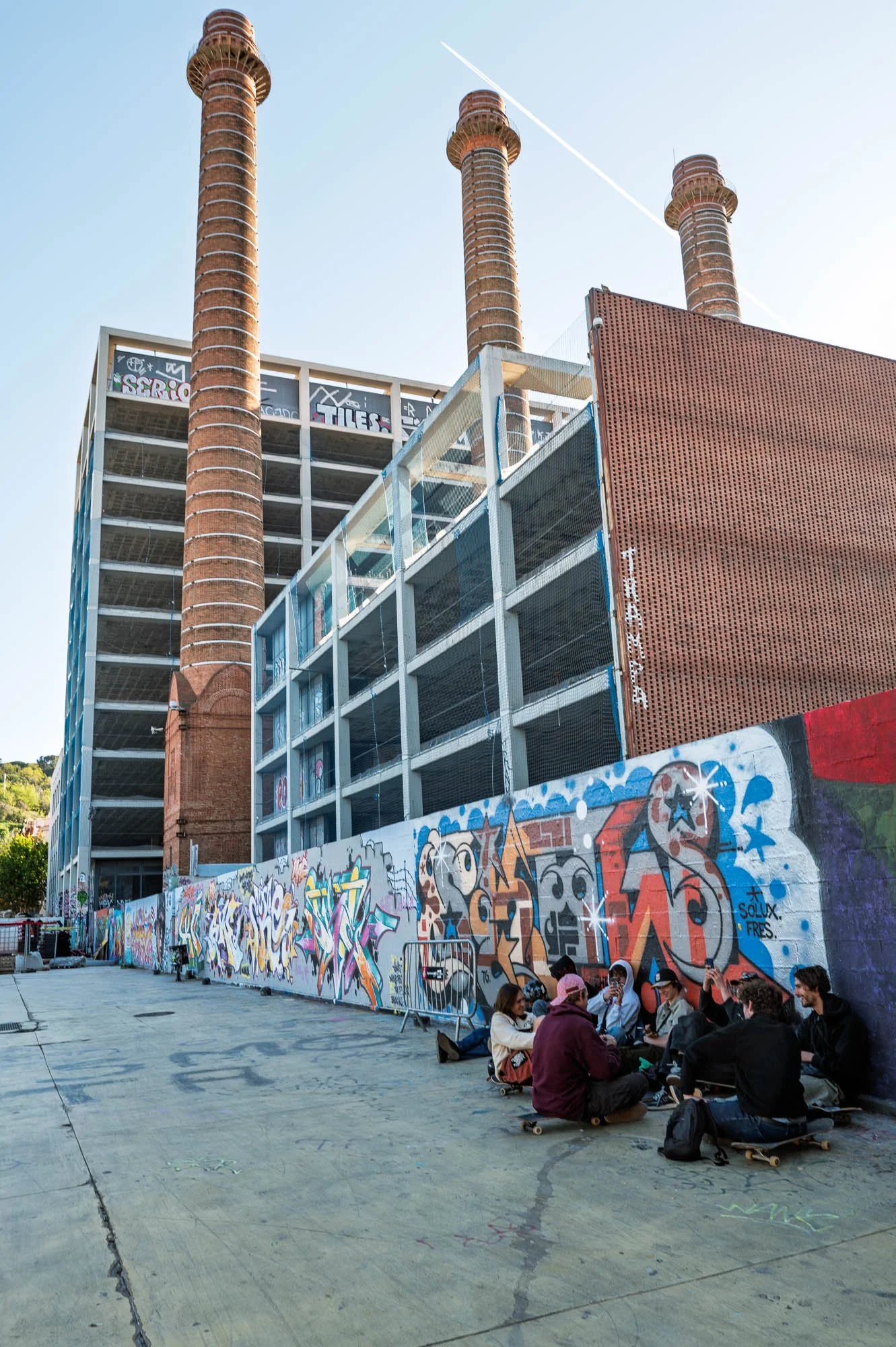 Skaters against a graffiti wall below the three brick chimneys of Parc de les Tres Xemeneies, Poble Sec — Leica Q3