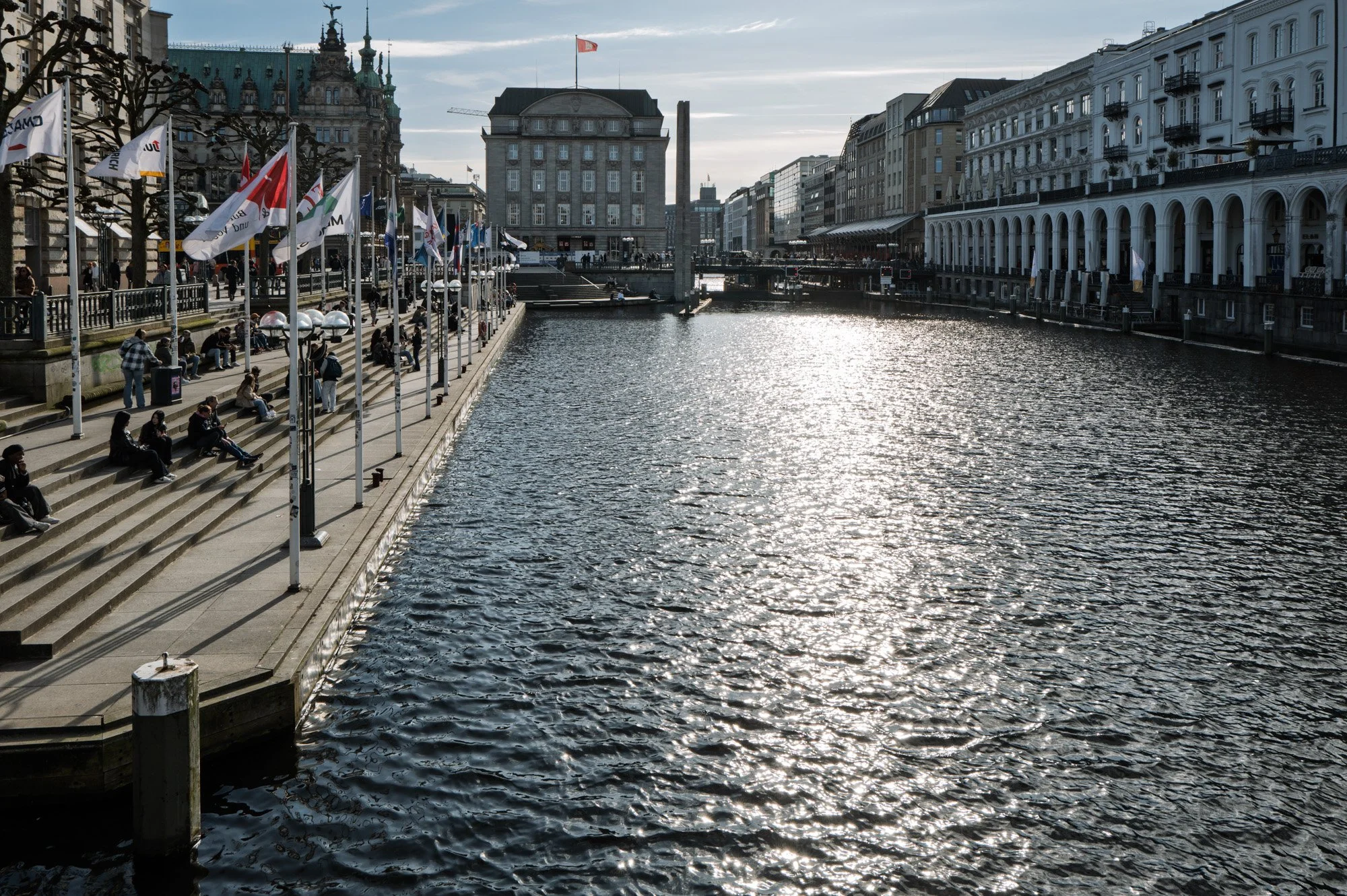 Winter afternoon light on the Alster canal with flags, terraced steps and Hamburg city hall in the background — bCLPhoto