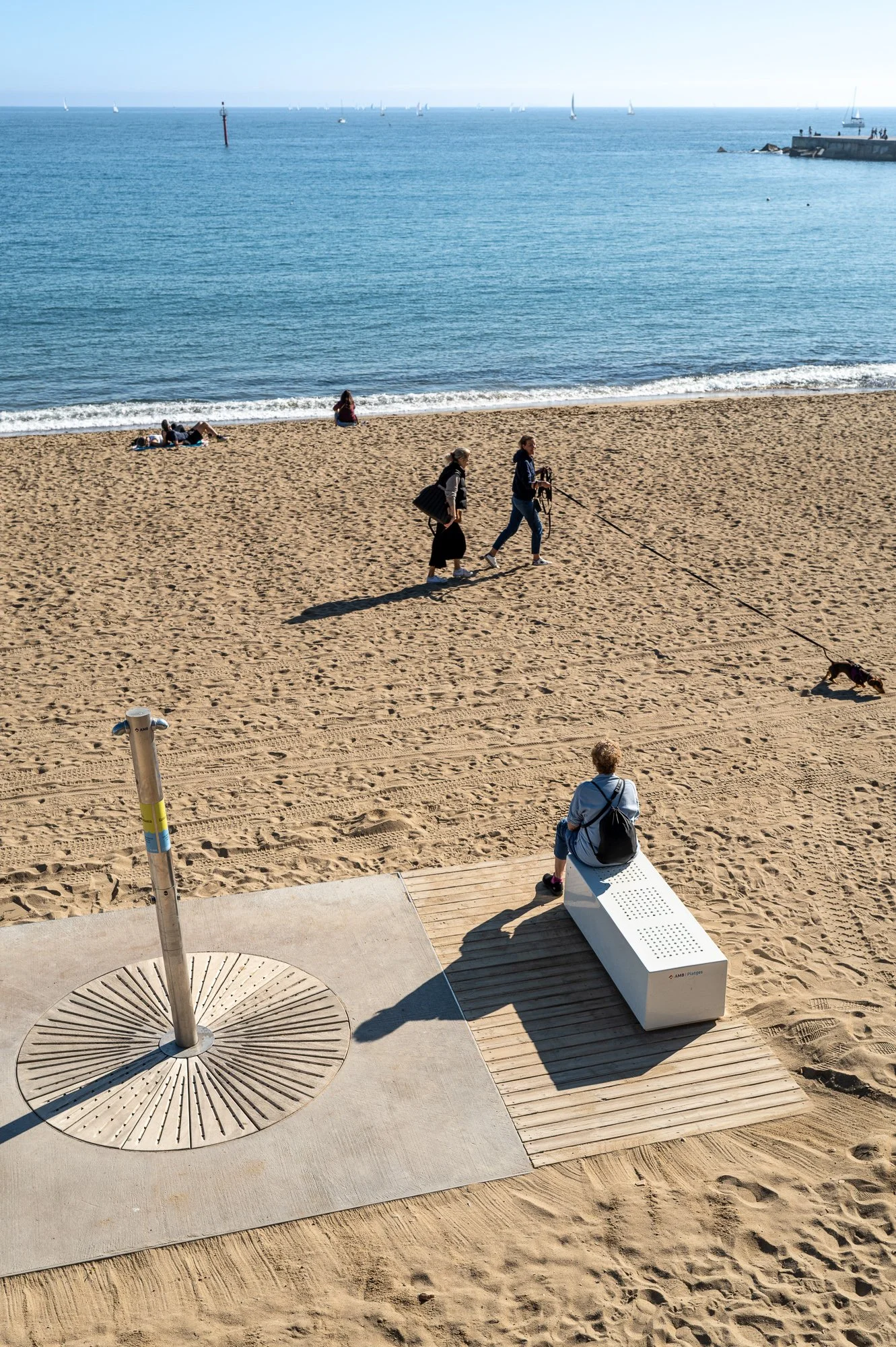 Beach shower, white bench and two women walking a dog, seen from above, Barceloneta — Leica Q3