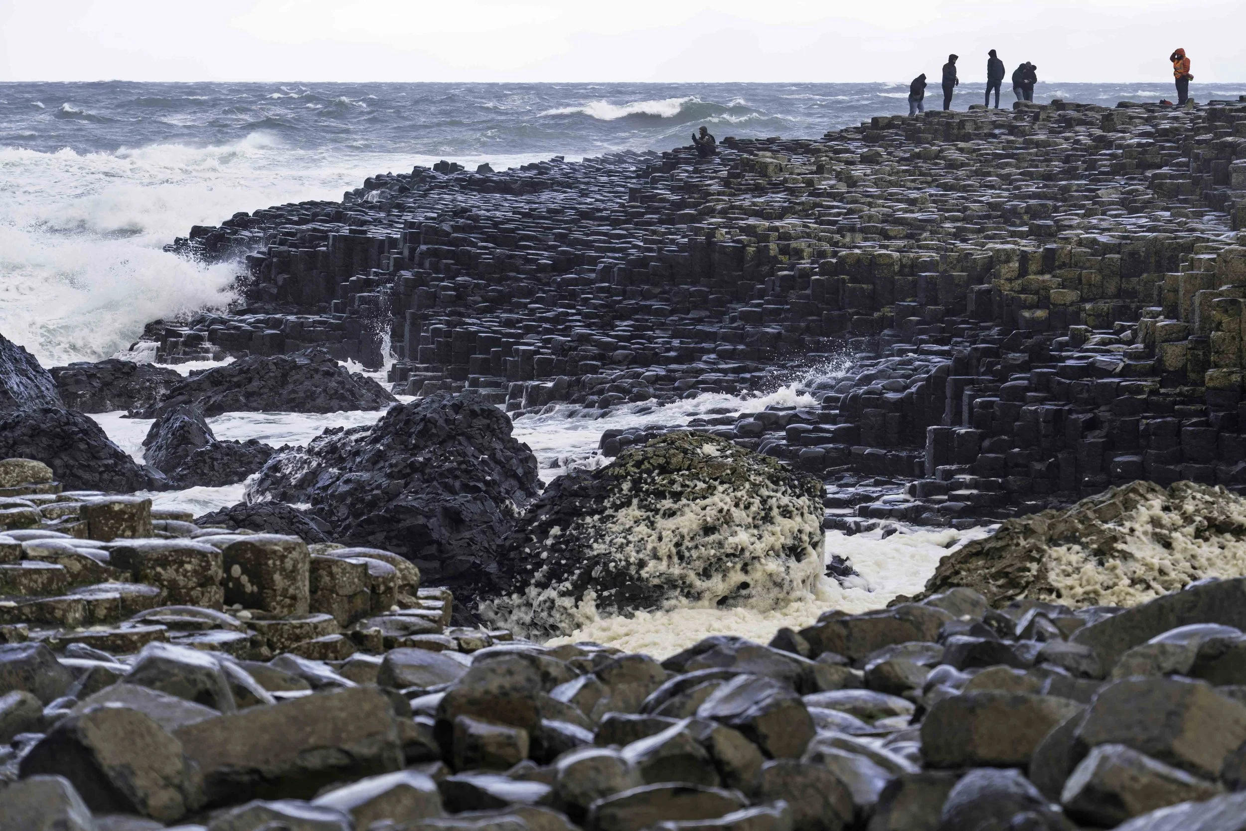 Visitors on the basalt columns at Giant's Causeway as powerful storm waves crash below, County Antrim, Northern Ireland – bCLPhoto