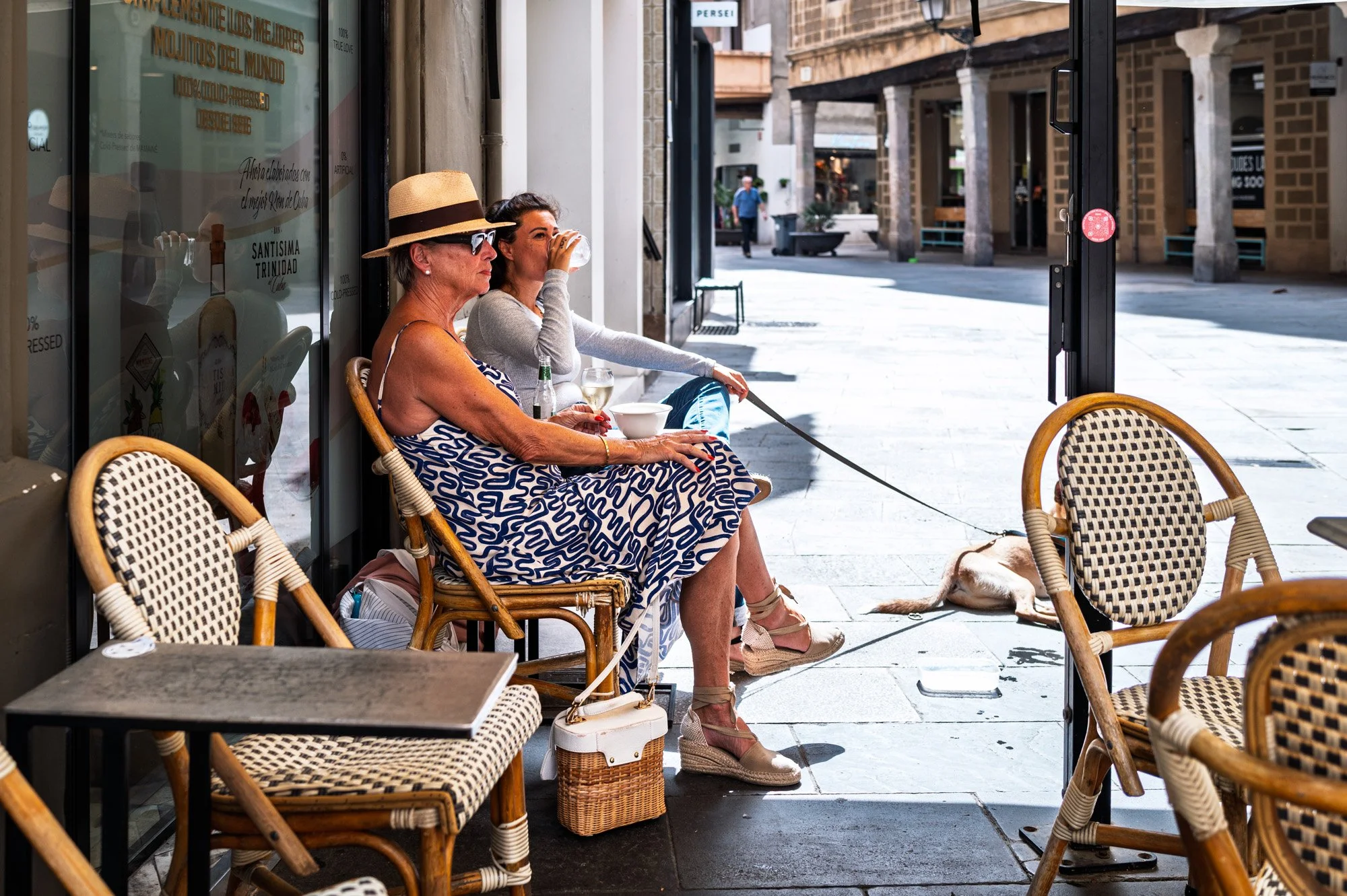Two women at a terrace table in El Born, Barcelona, with a dog resting nearby under the arcades