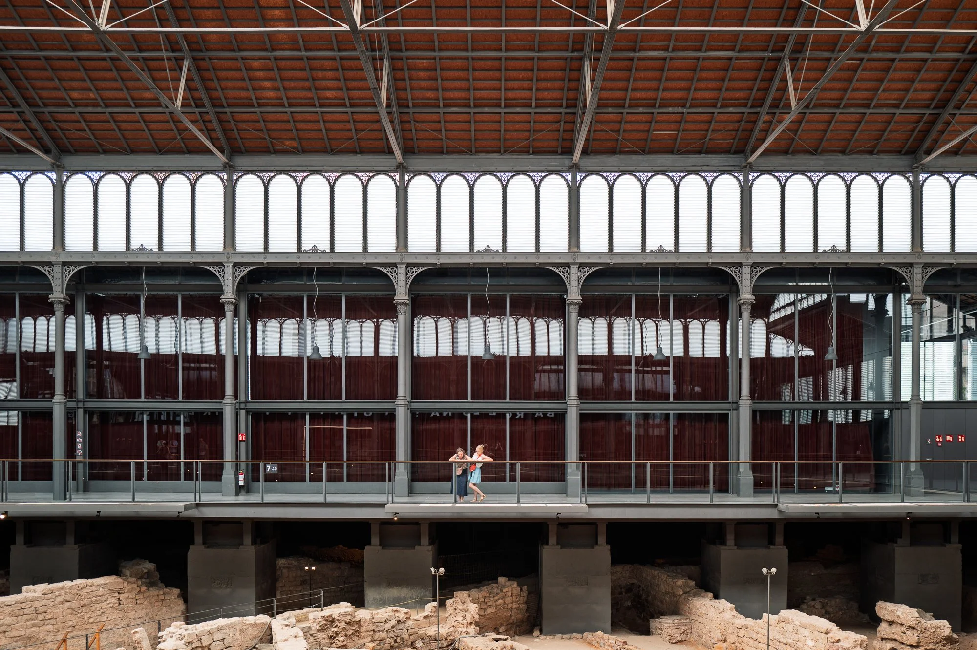 Two visitors leaning on the walkway rail above the Mercat del Born ruins — Leica Q3