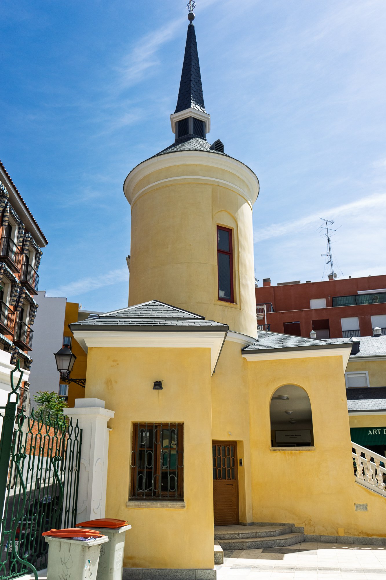 Yellow round tower with a slate spire at the entrance to Galerías Piquer, a green iron gate on the left, Madrid