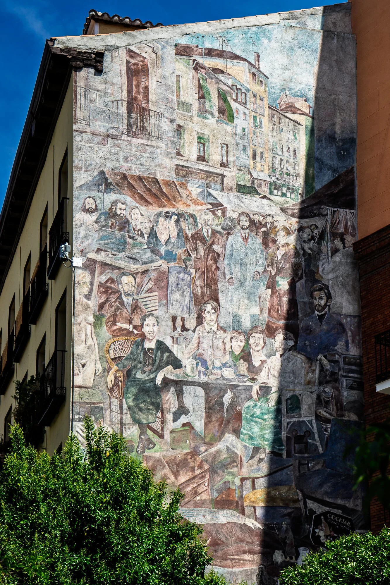 Large mural on a party wall at Plaza de Cascorro showing market awnings and a crowd of faces at café tables, Madrid
