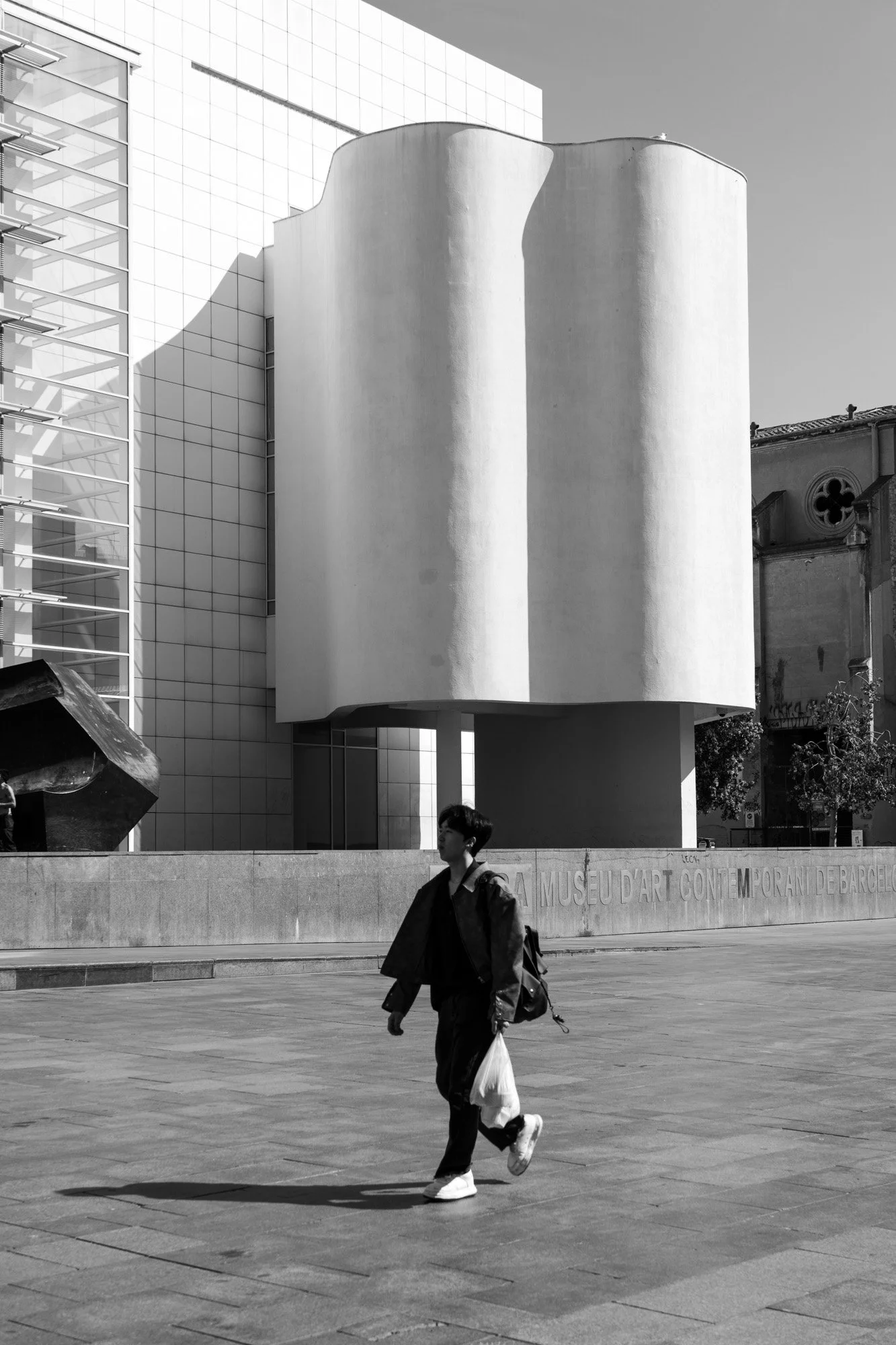 Man walking past MACBA curved facade, old church behind — Sony A7R IV
