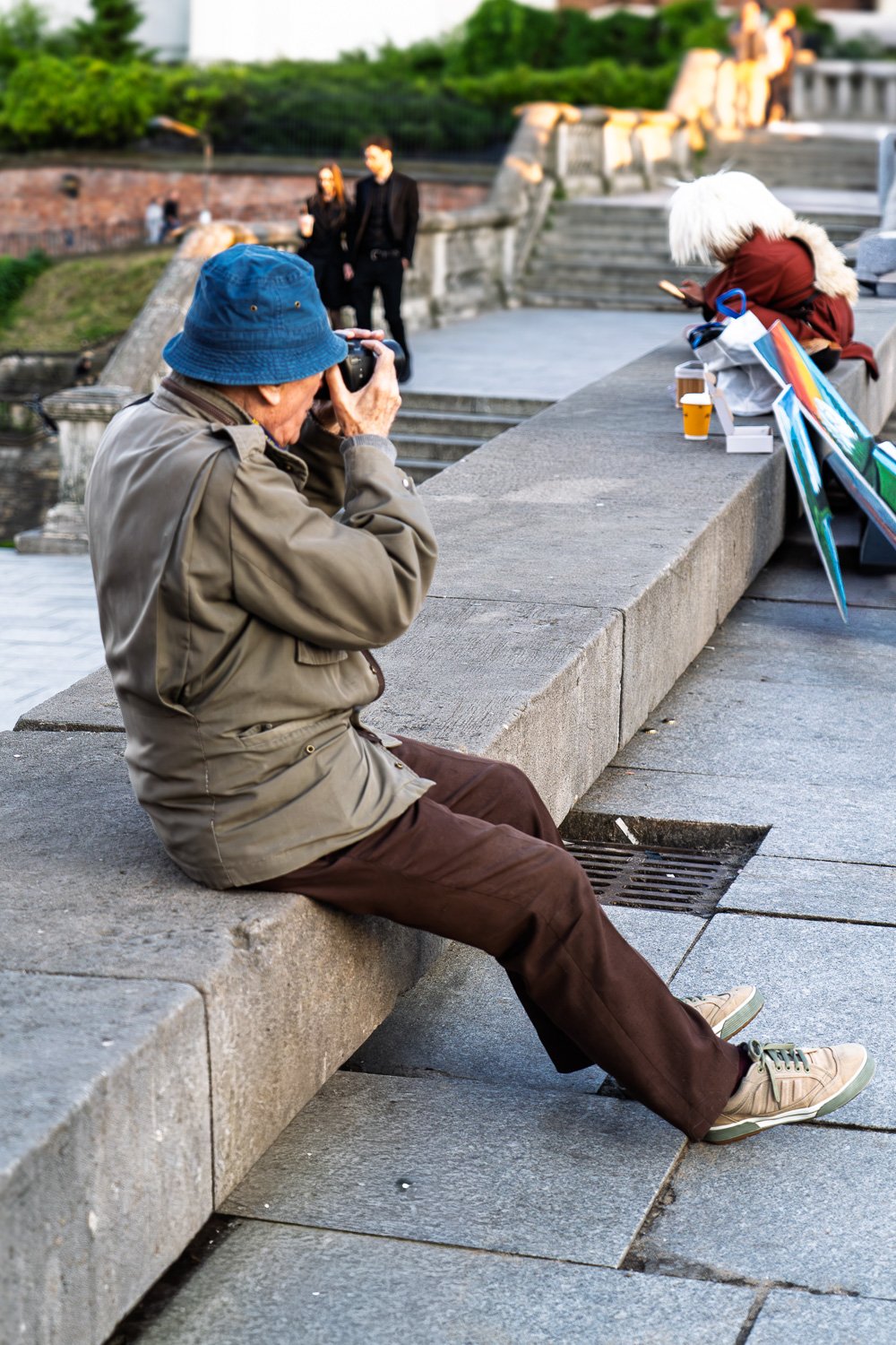 Older man in a blue bucket hat photographing from a stone balustrade, Castle Square, Warsaw — Sony a7R IV