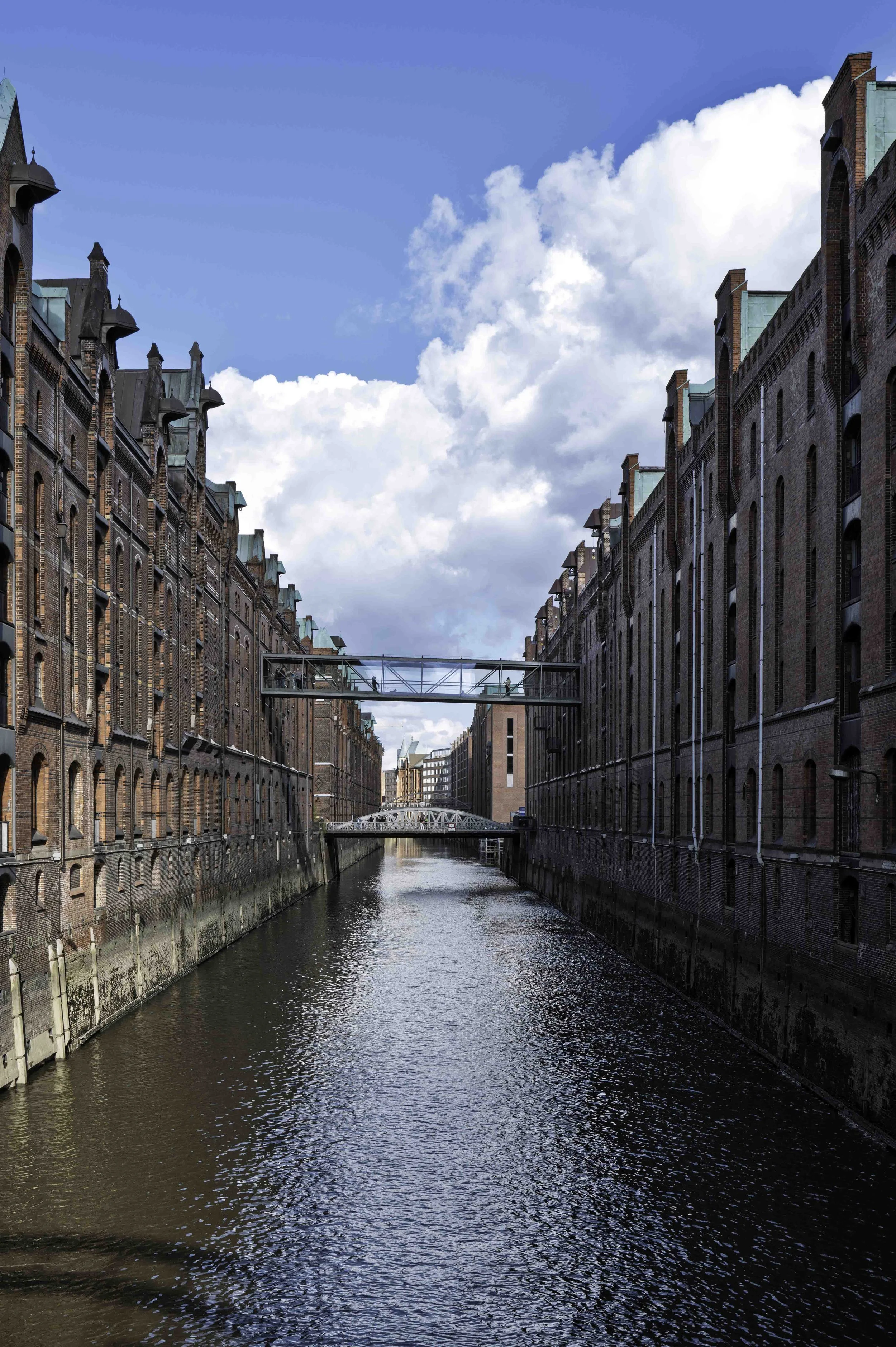 Deep canal perspective in Hamburg Hafencity district with two arch bridges receding into the distance, warm side light — Leica Q3