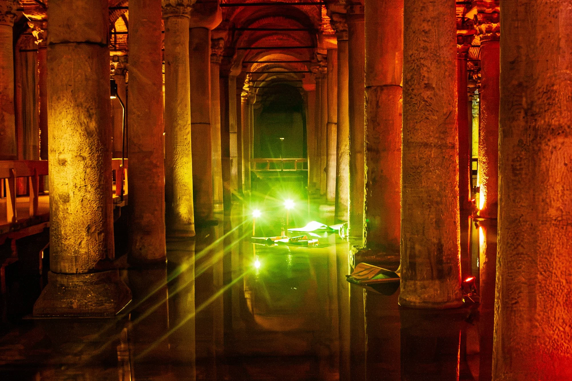 Green lights and floating sheets between amber columns in the Basilica Cistern, light rays across the water