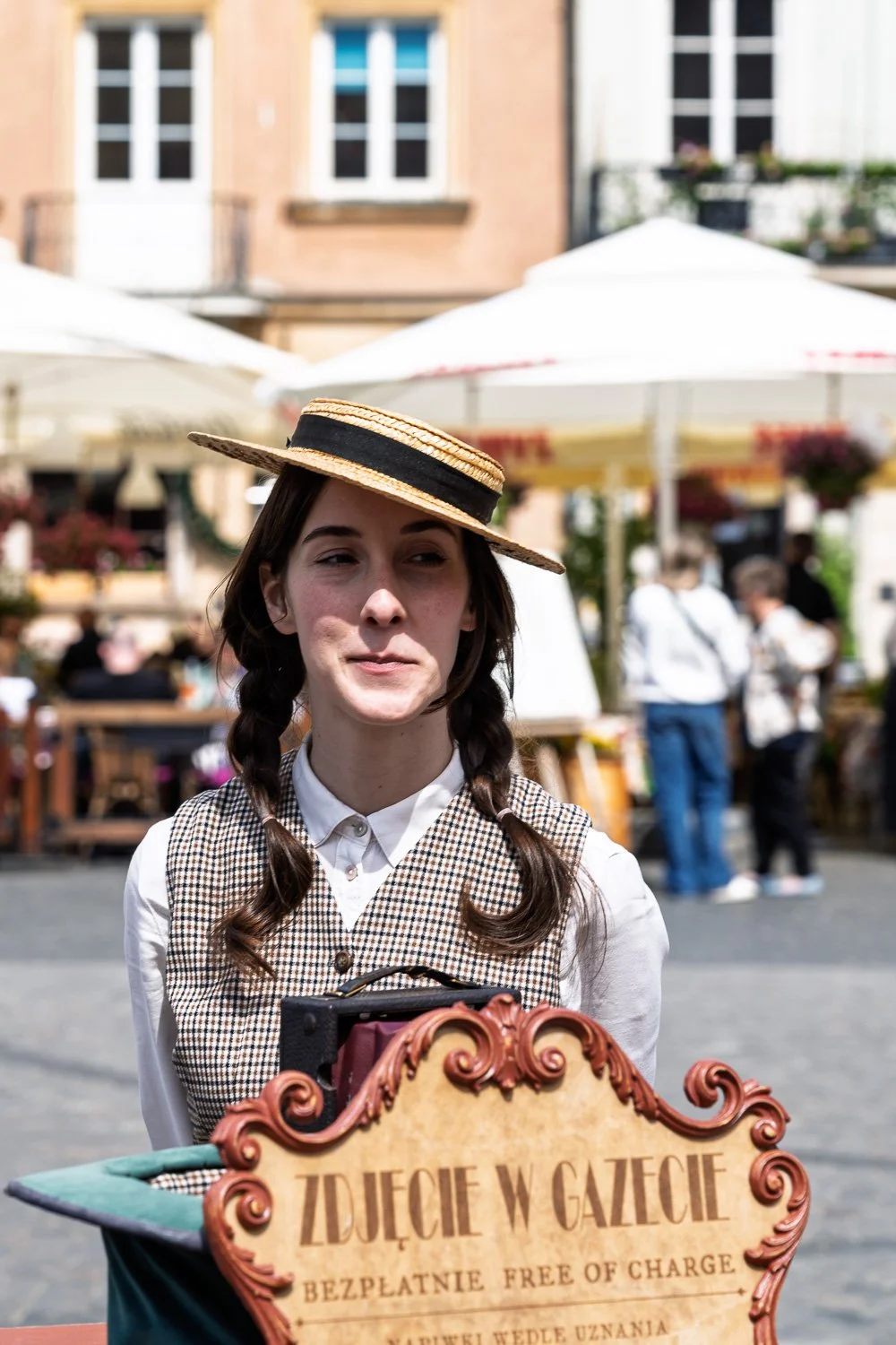 Woman in a straw boater and braids behind a vintage camera and ornate sign, Market Square, Warsaw — Sony a7R IV