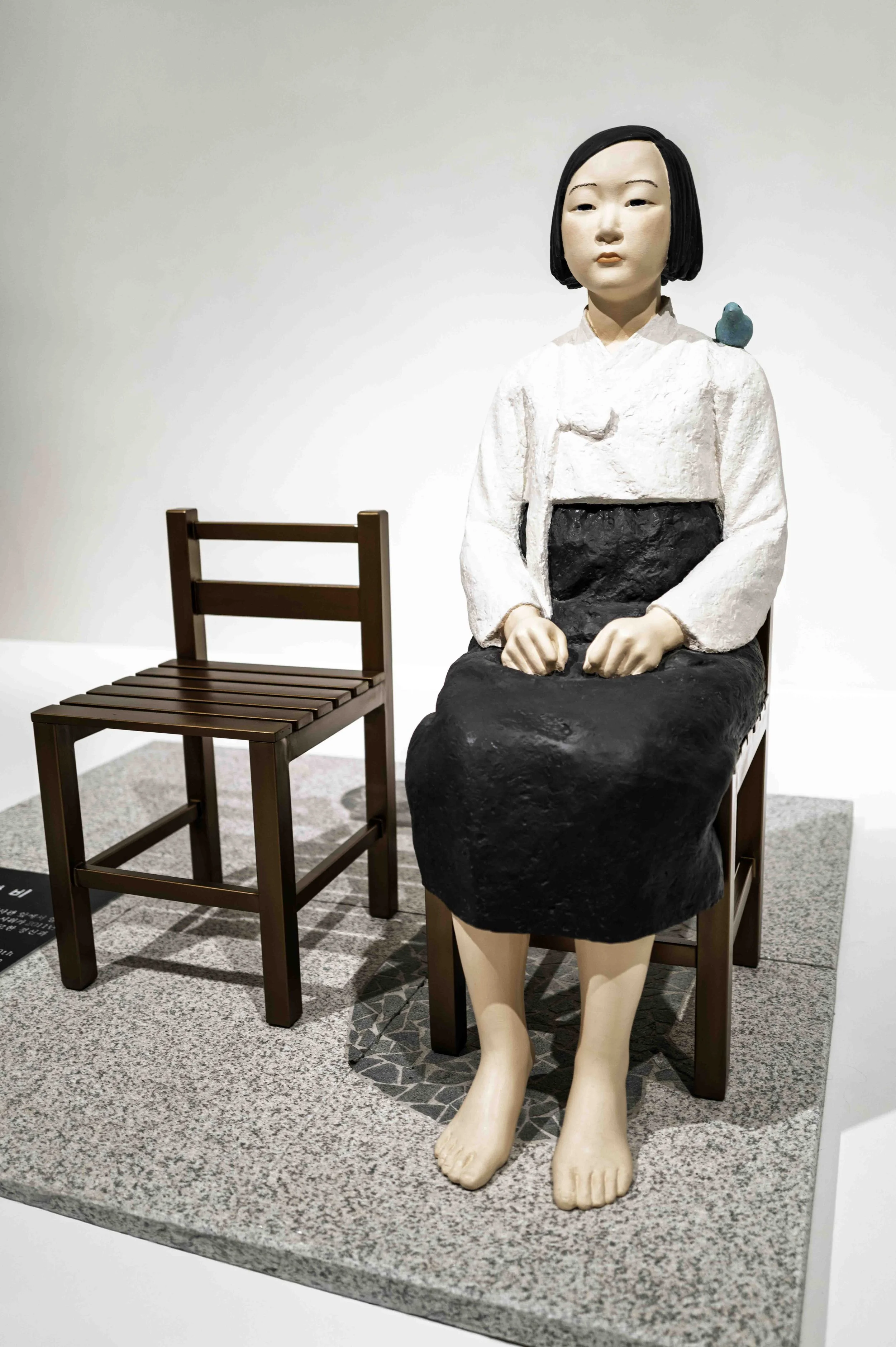 Girl of Peace sculpture seated with empty chair beside her, Museum of Forbidden Art Barcelona — Leica Q3