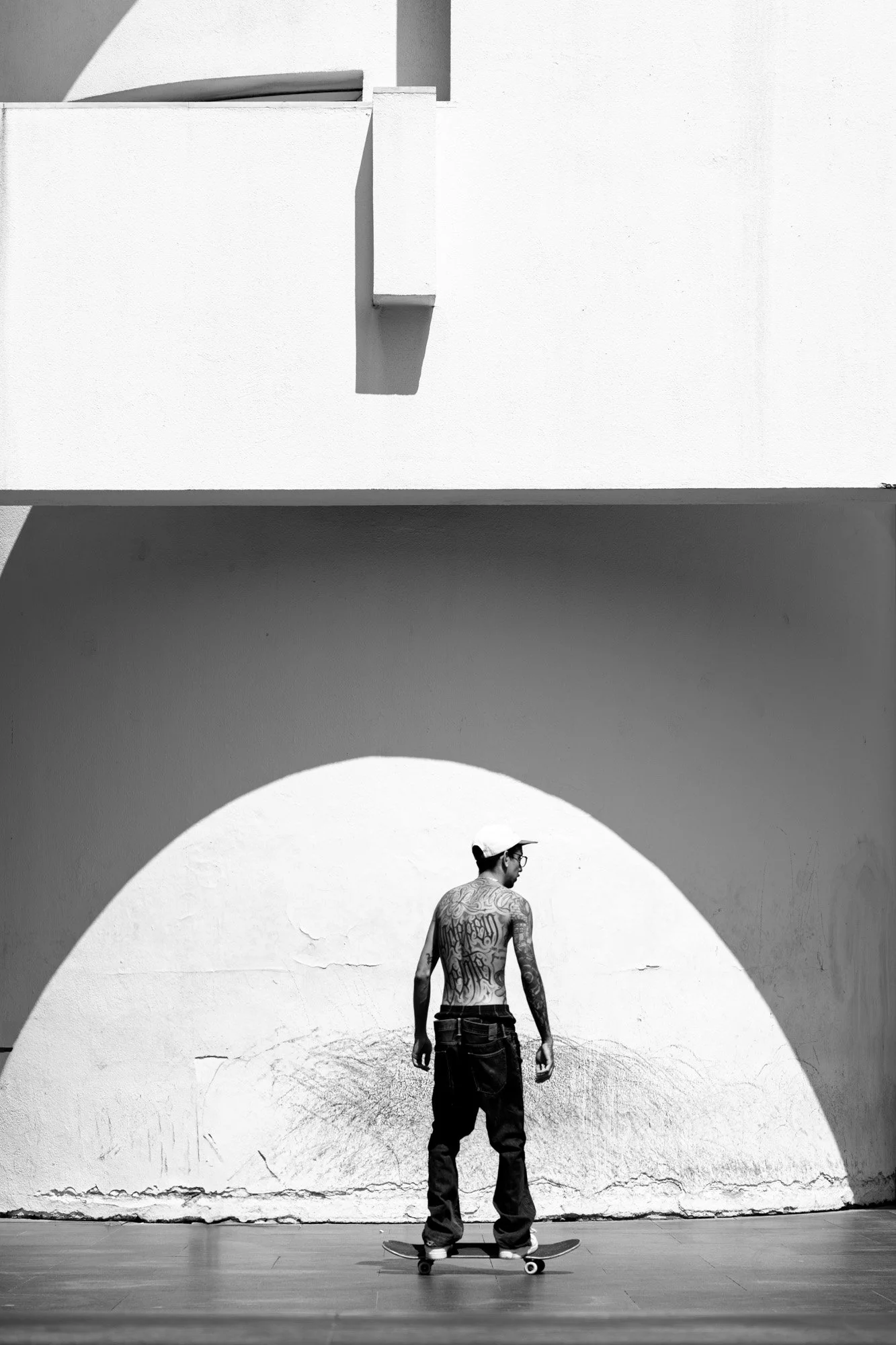 Skateboarder standing before a white semicircular shadow at MACBA Barcelona, black and white urban photography — Sony a7R IV