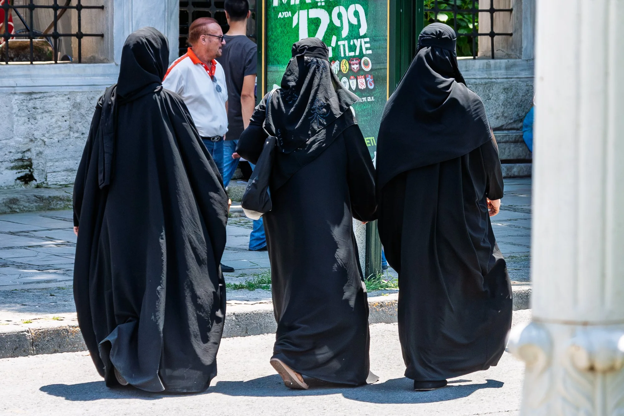 Three women in black çarşaf and niqab walking past a green billboard, Istanbul — Canon EOS 40D