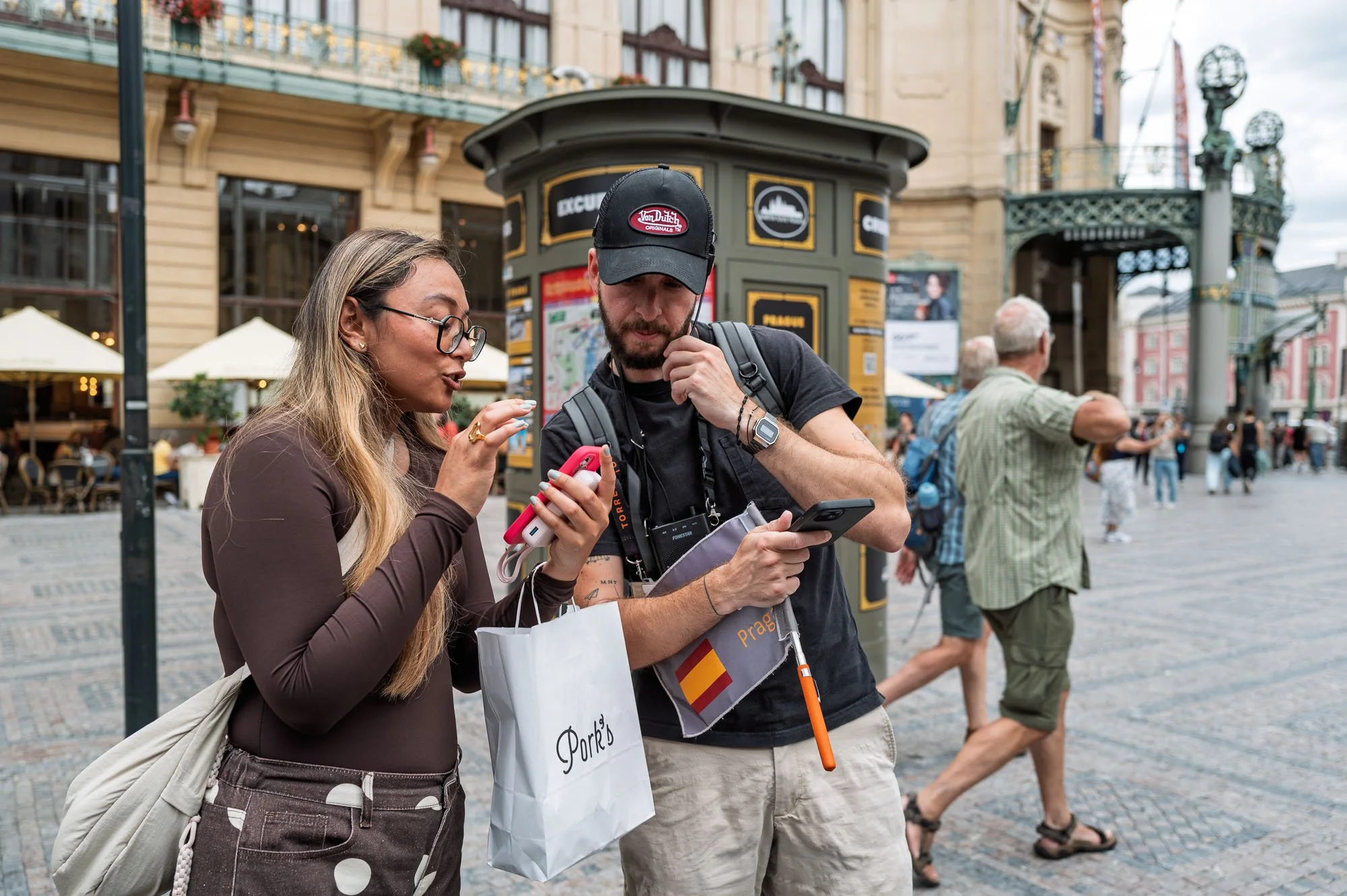 Free-tour guide with a Spanish flag on an orange pole answering a young woman's question, Prague — Leica Q3