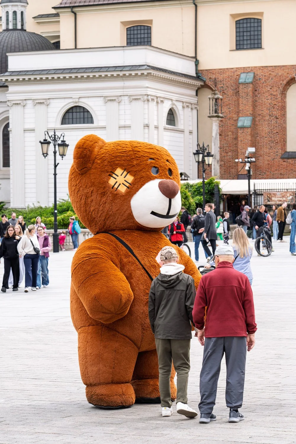 Giant teddy bear costume facing an older man and a boy seen from behind, Warsaw Old Town — Sony a7R IV