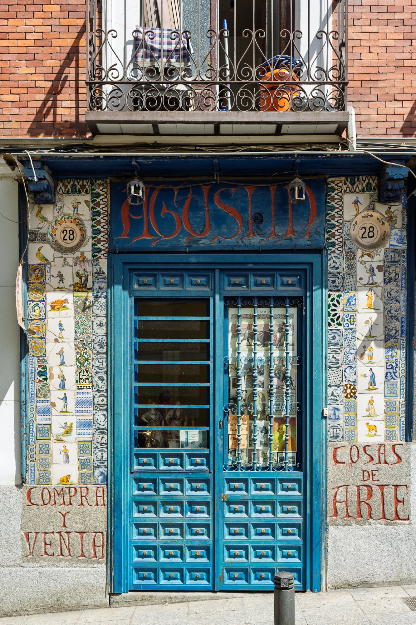 Blue wooden doors of an antique shop named Agustín, framed by hand-painted tiles, with Compra y venta carved in stone
