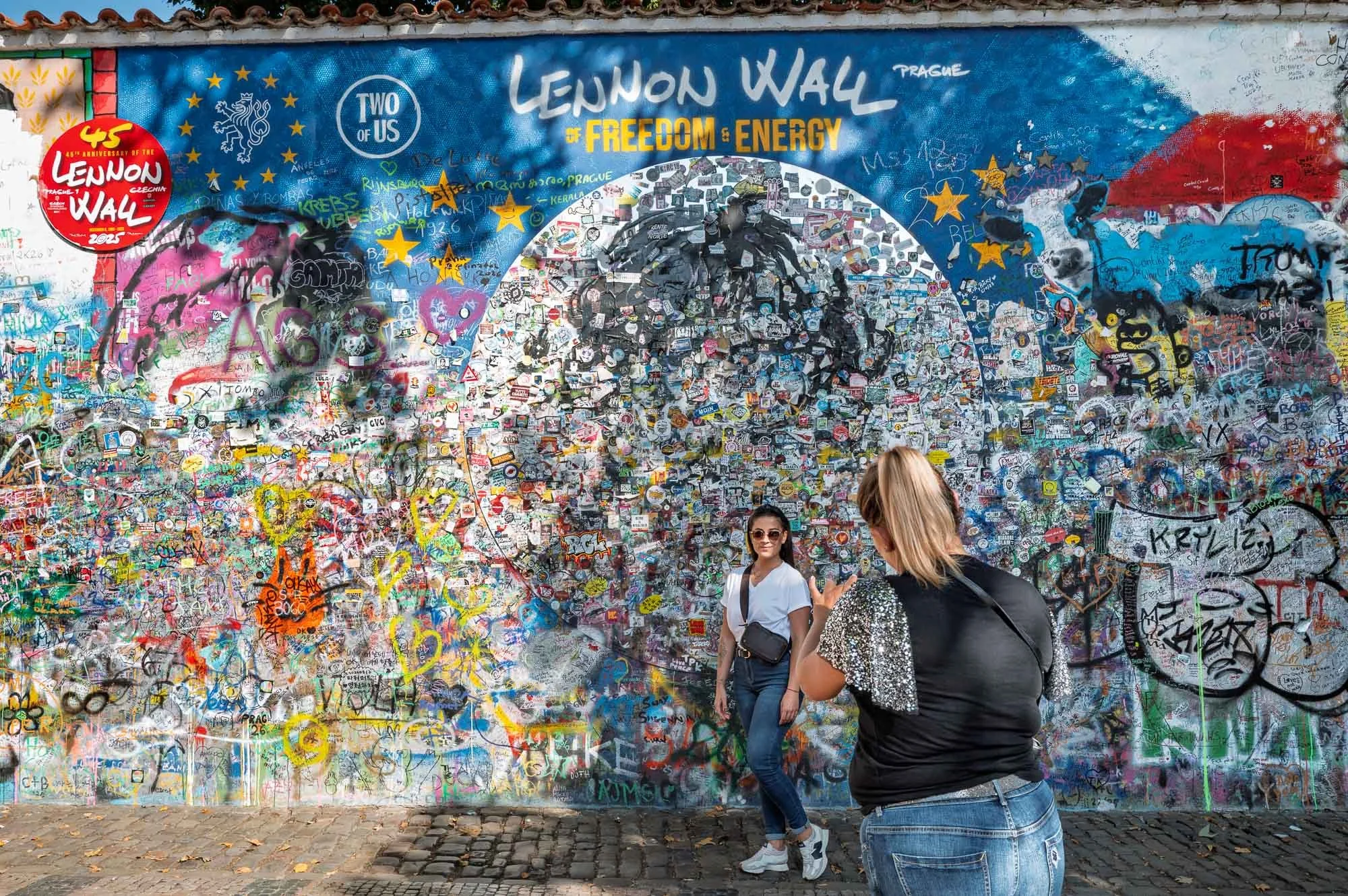 Woman posing at the Lennon Wall while her friend directs the shot, Prague — Leica Q3