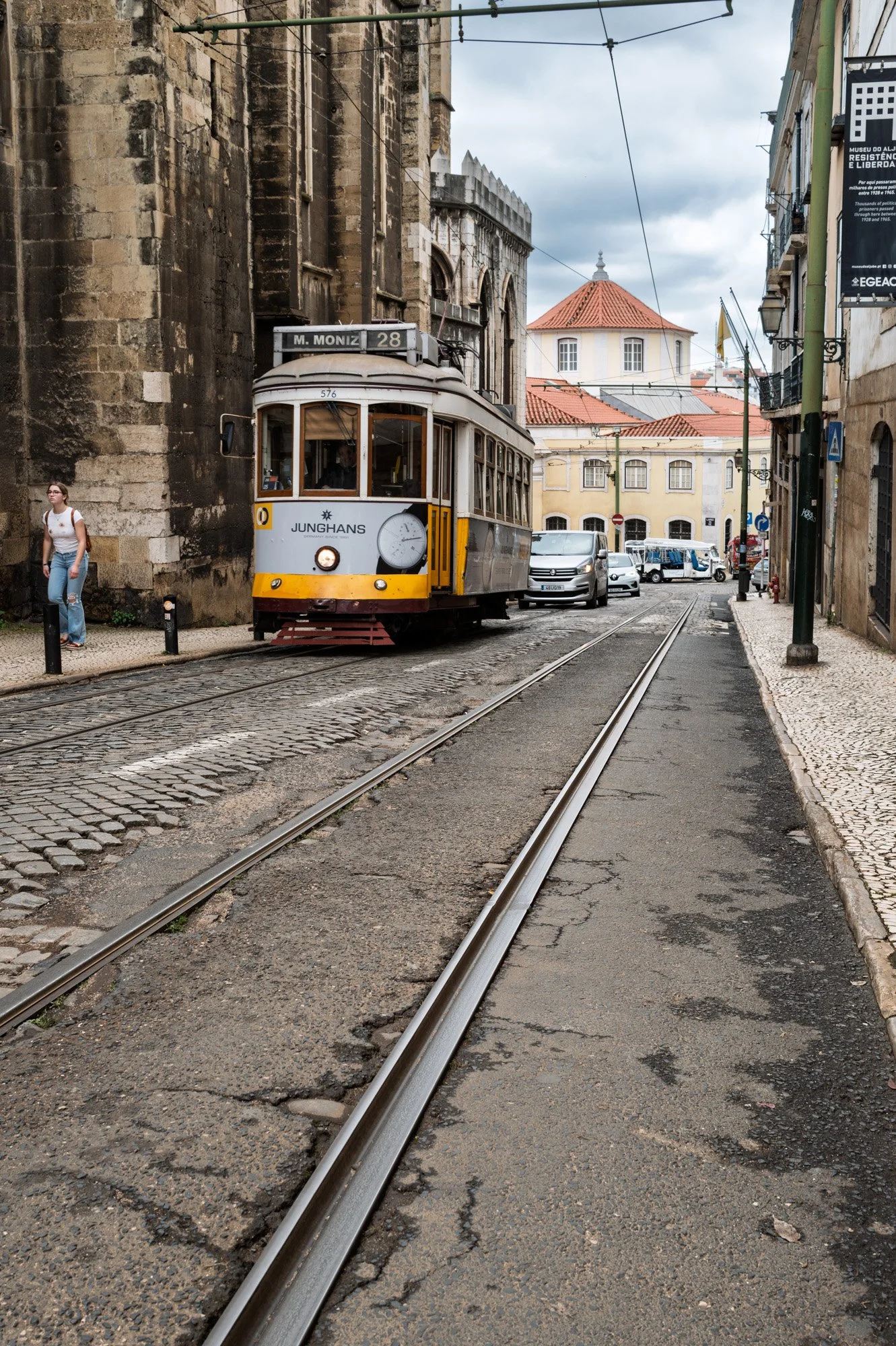Yellow tram 28 navigating a narrow cobblestone street beside a Gothic church wall, Alfama, Lisbon — bCLPhoto
