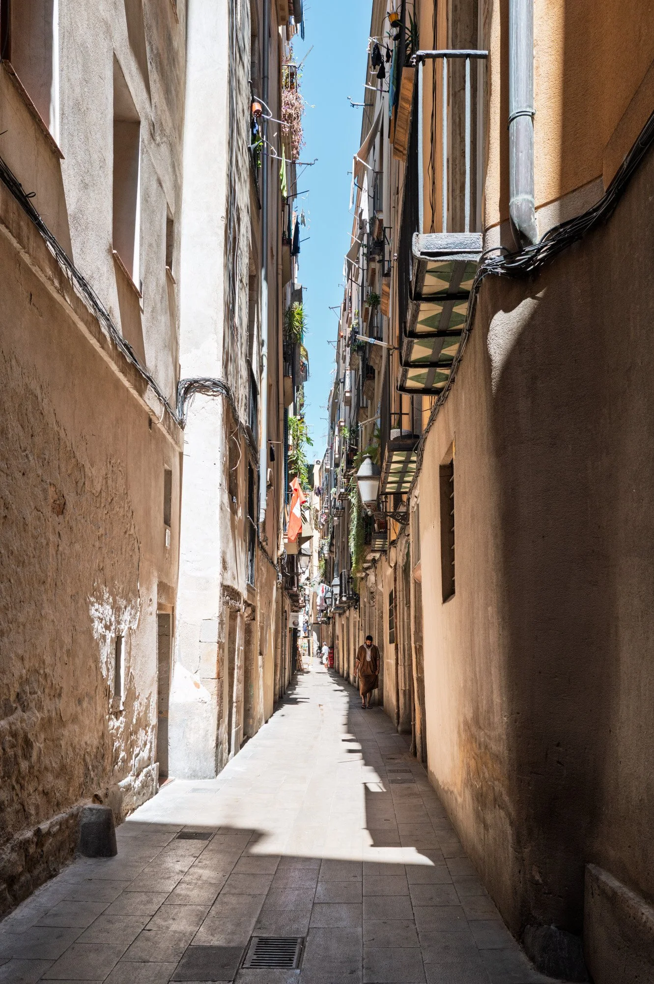 Man in a brown djellaba walking past a shuttered shop grille, El Born — Leica Q3